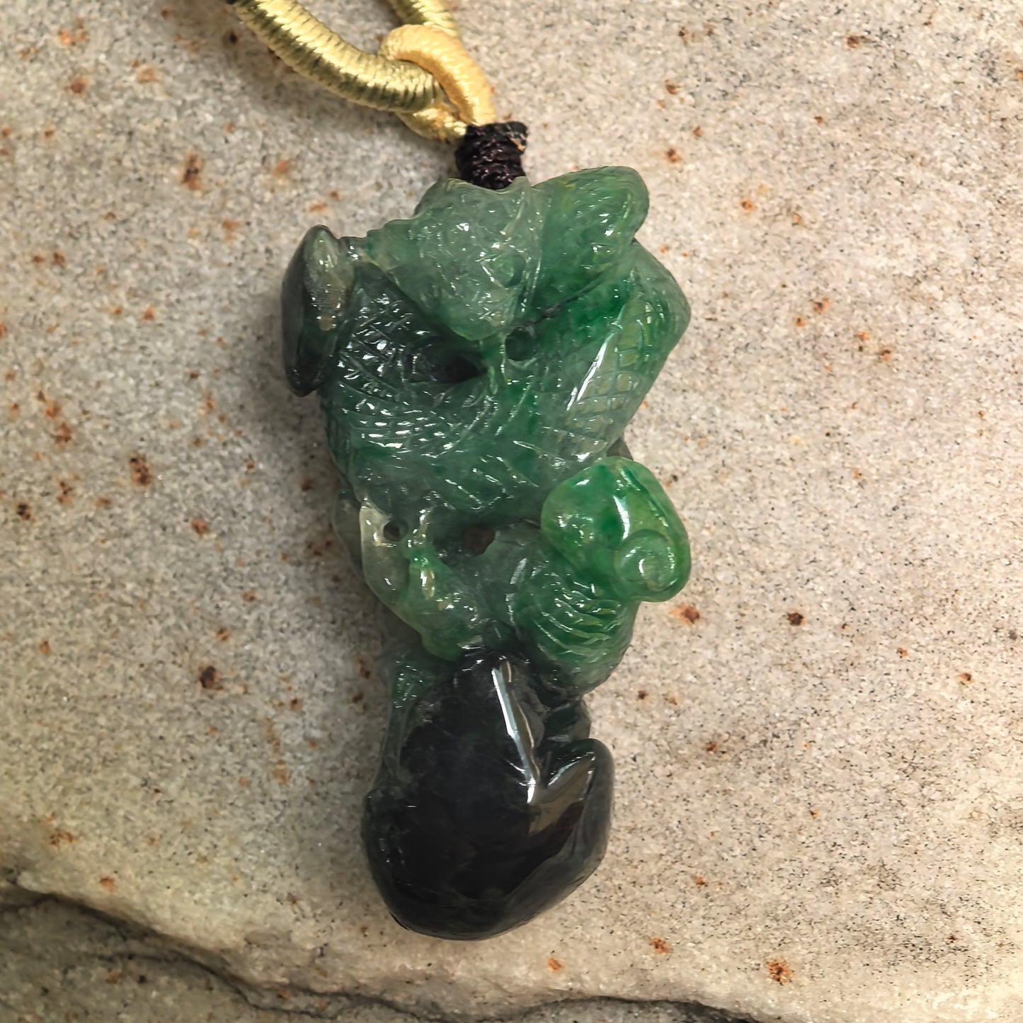 Close-up of green and black jadeite snake pendant showing carved head, coiled form, and glossy polish.