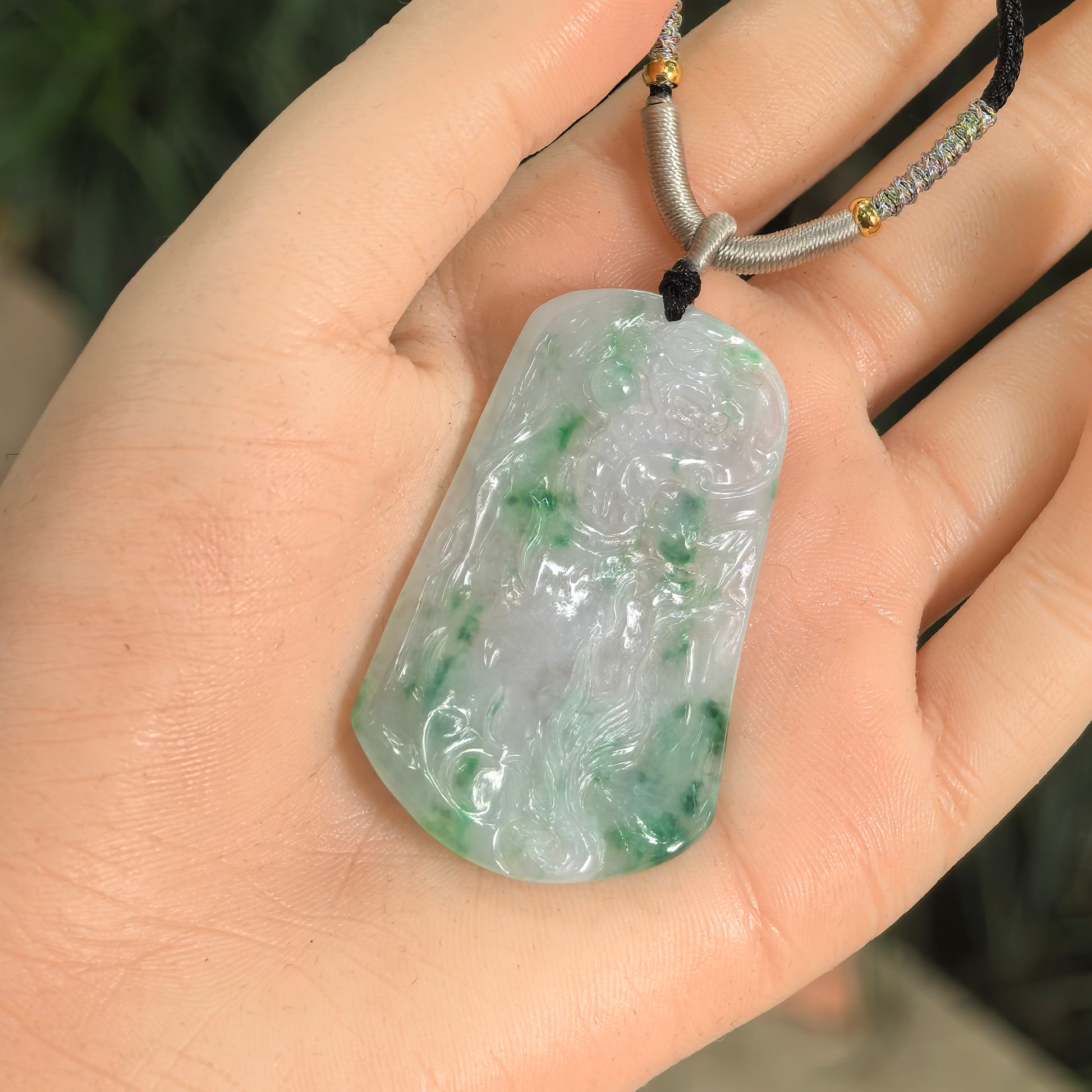 Pale green jadeite dragon pendant shown in hand with natural green floating color and glossy surface.