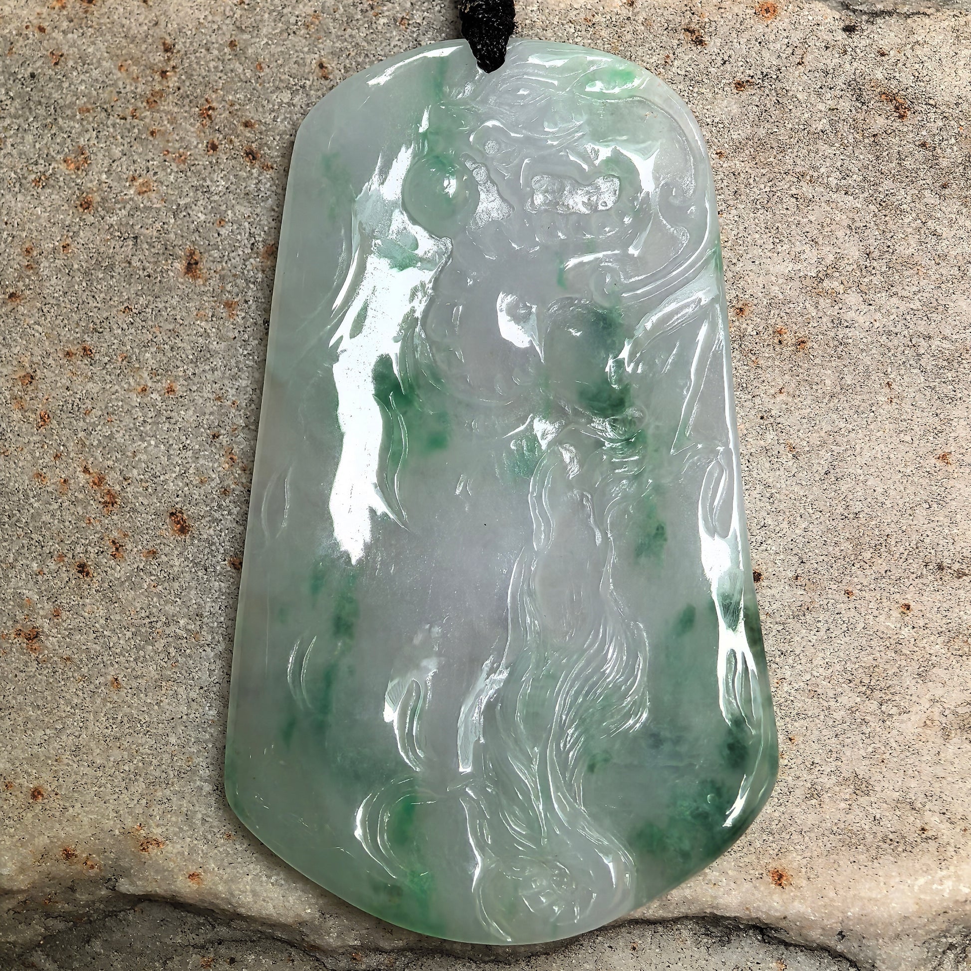 Close-up of carved jadeite dragon pendant showing icy luster and slim plaque-style shape.