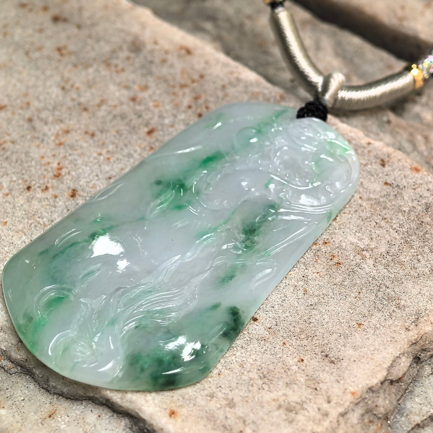 Angled view of green floating color jadeite pendant with detailed dragon carving and good translucency.
