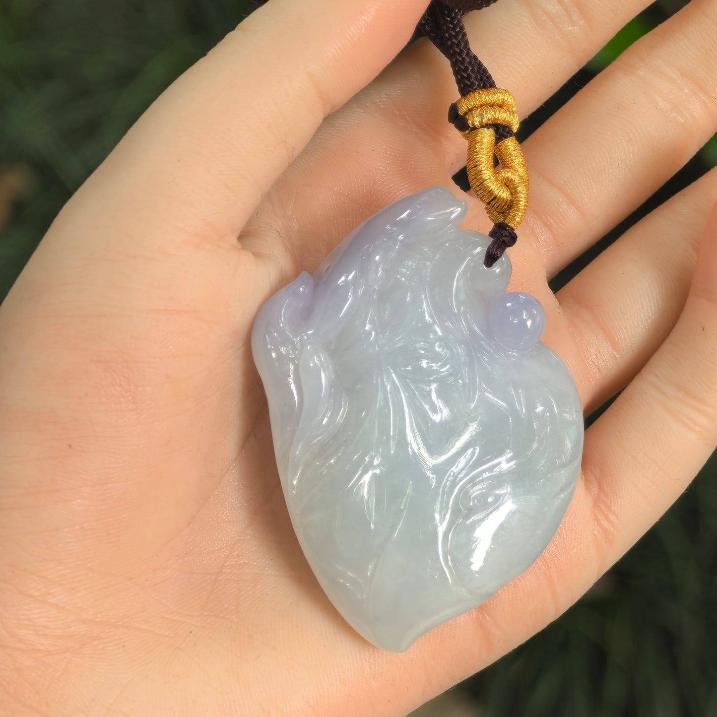 Carved jadeite dolphin pendant shown in hand with soft light purple and light green tones.