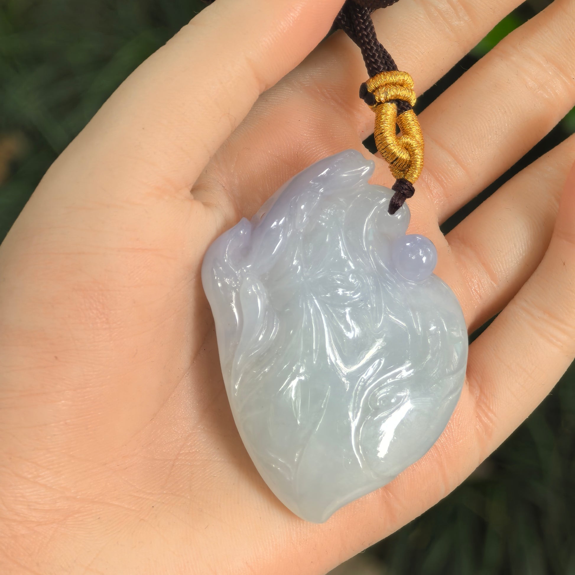 Carved jadeite dolphin pendant shown in hand with soft light purple and light green tones.