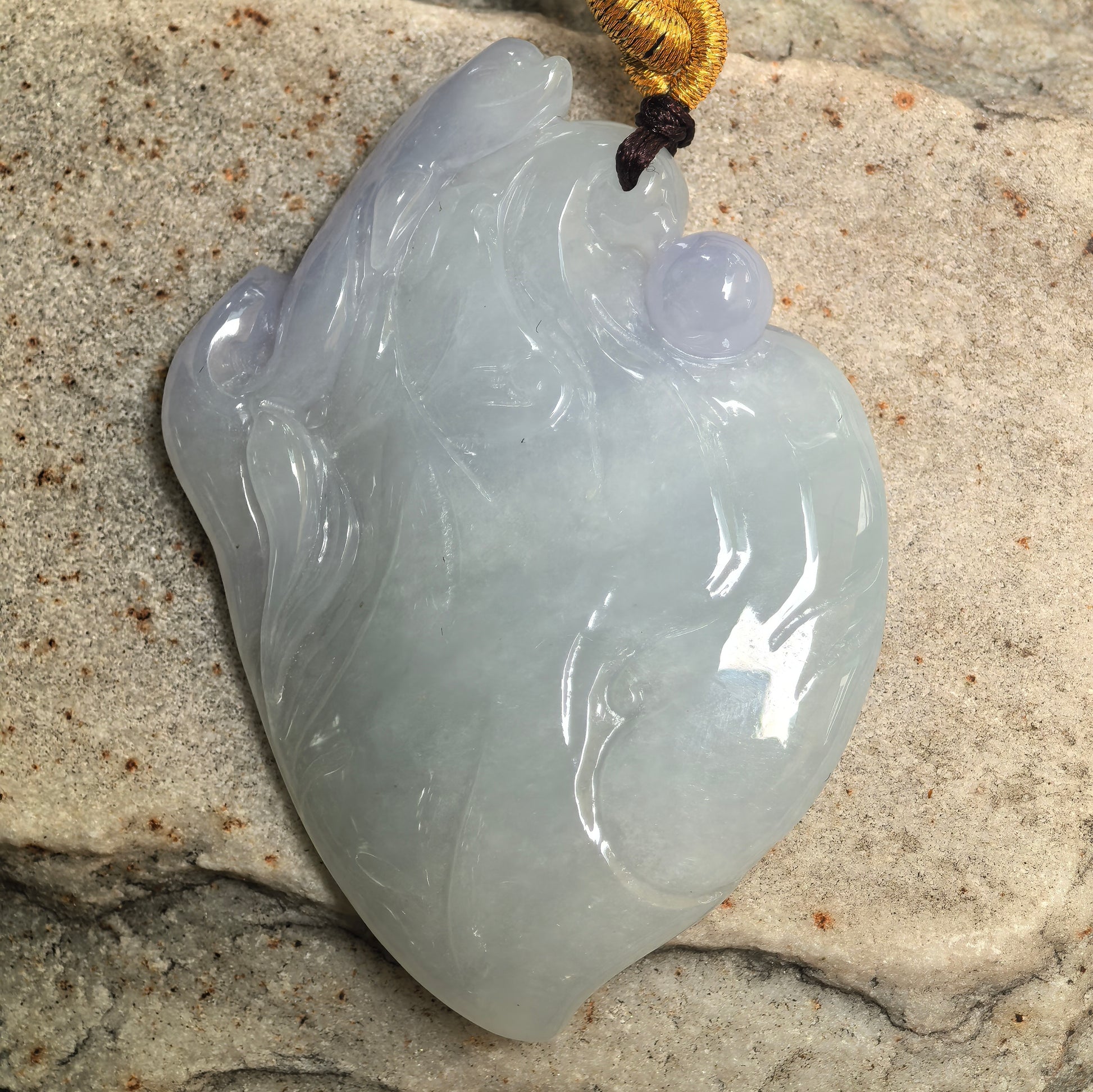 Close-up of dolphin riding wave jadeite pendant showing glossy polish and gelatinous texture.