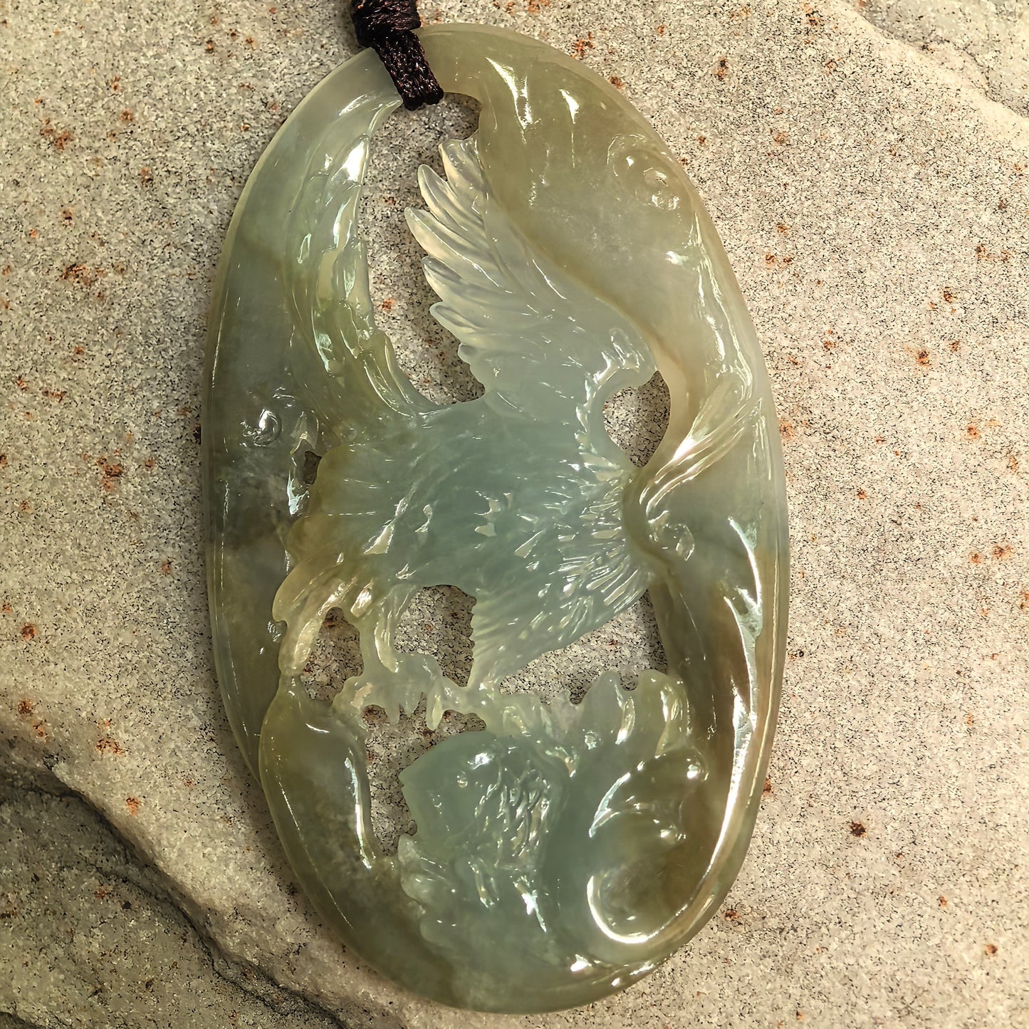 Close-up of openwork jadeite eagle pendant showing detailed wings and fish carving.