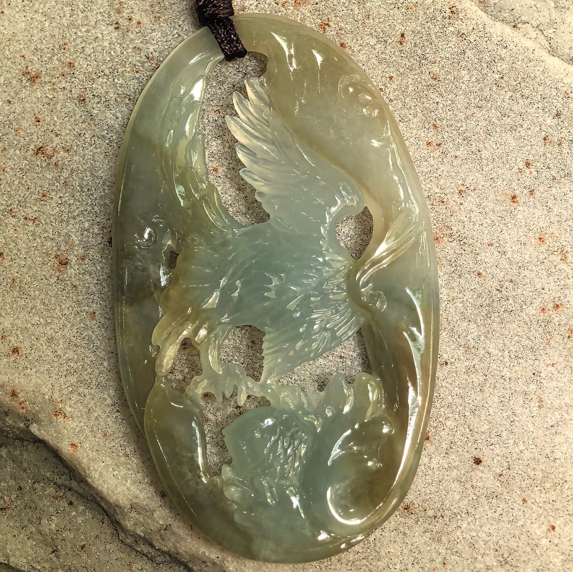 Close-up of openwork jadeite eagle pendant showing detailed wings and fish carving.