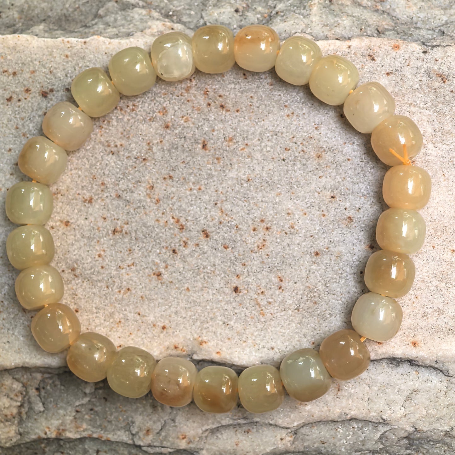 Natural Hetian jade bracelet with warm caramel and pale yellow bead tones displayed on stone background.