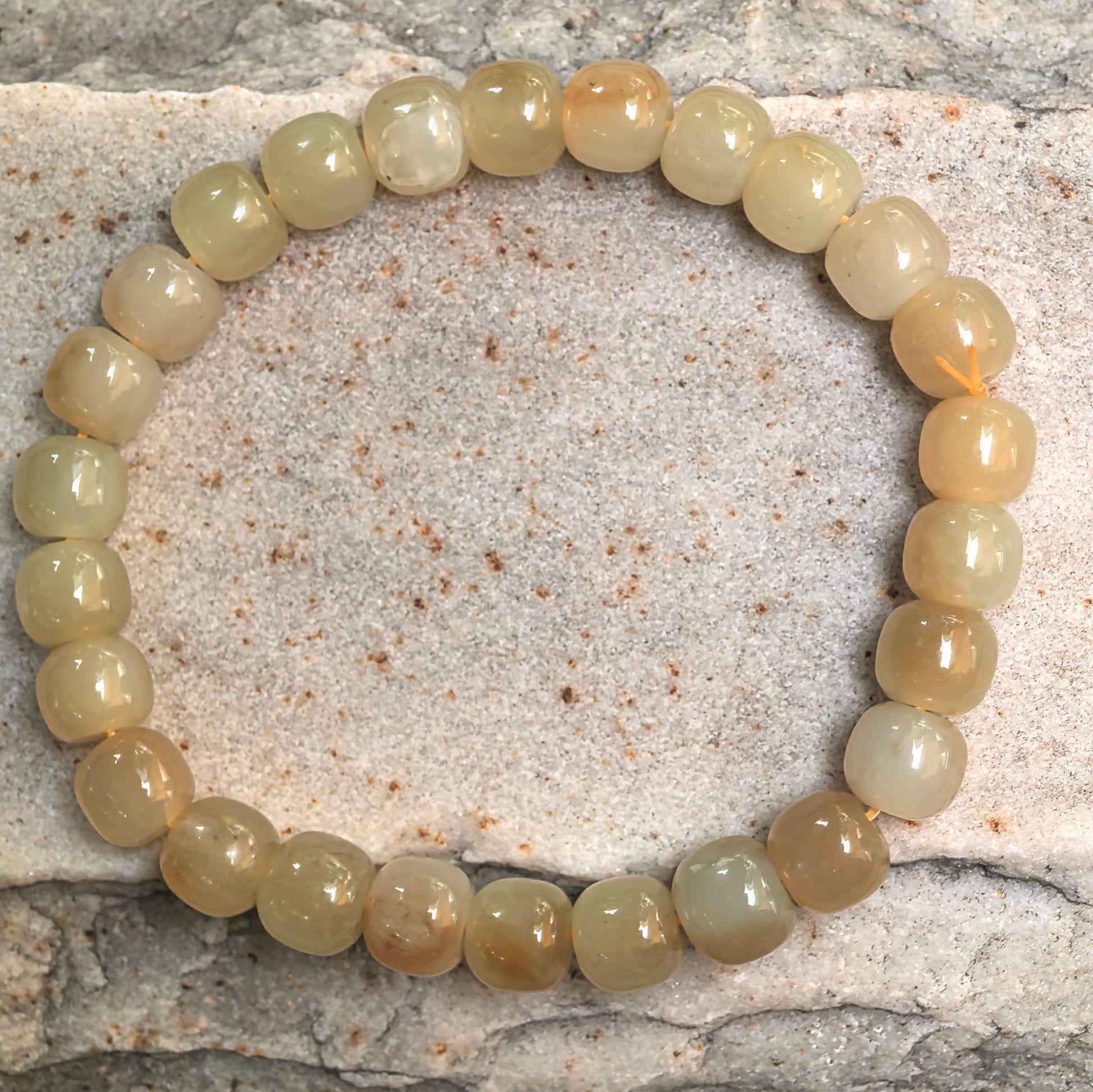 Natural Hetian jade bracelet with warm caramel and pale yellow bead tones displayed on stone background.