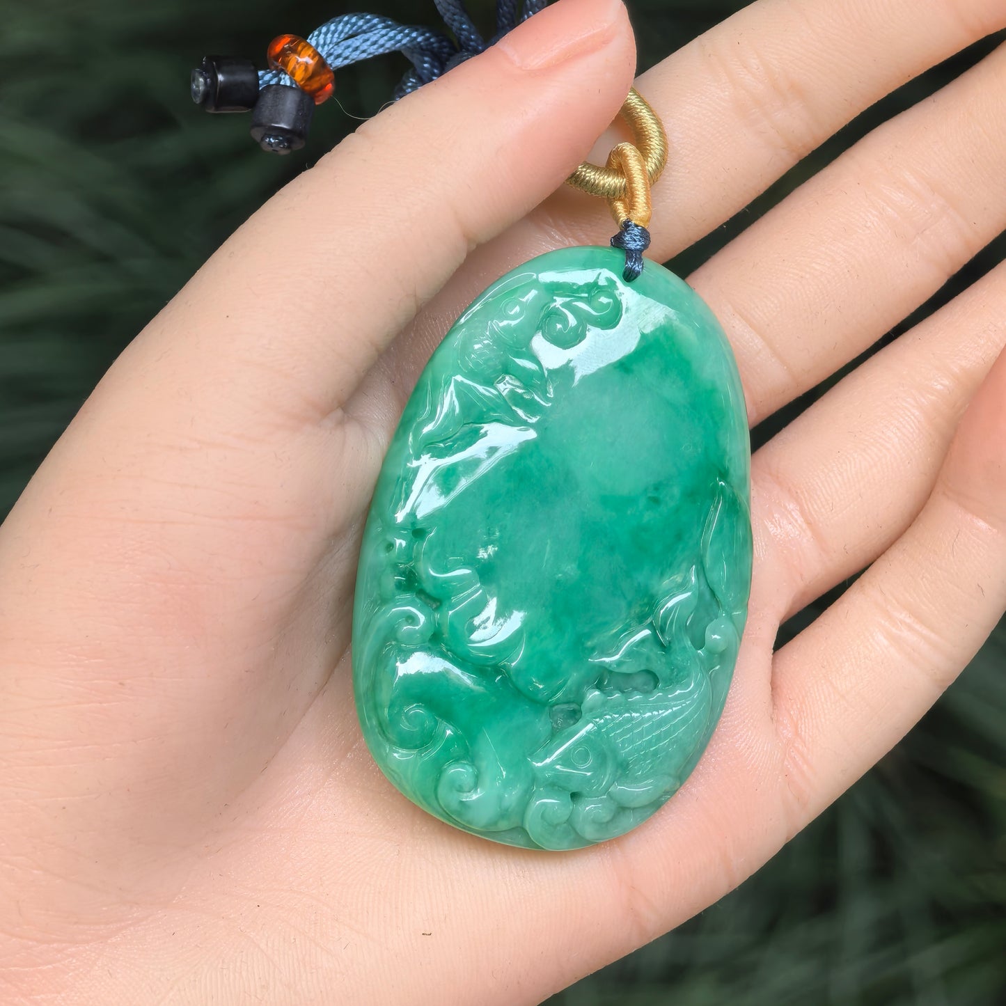 Large green jadeite plaque pendant shown in hand with carved fish and flowing water motif.