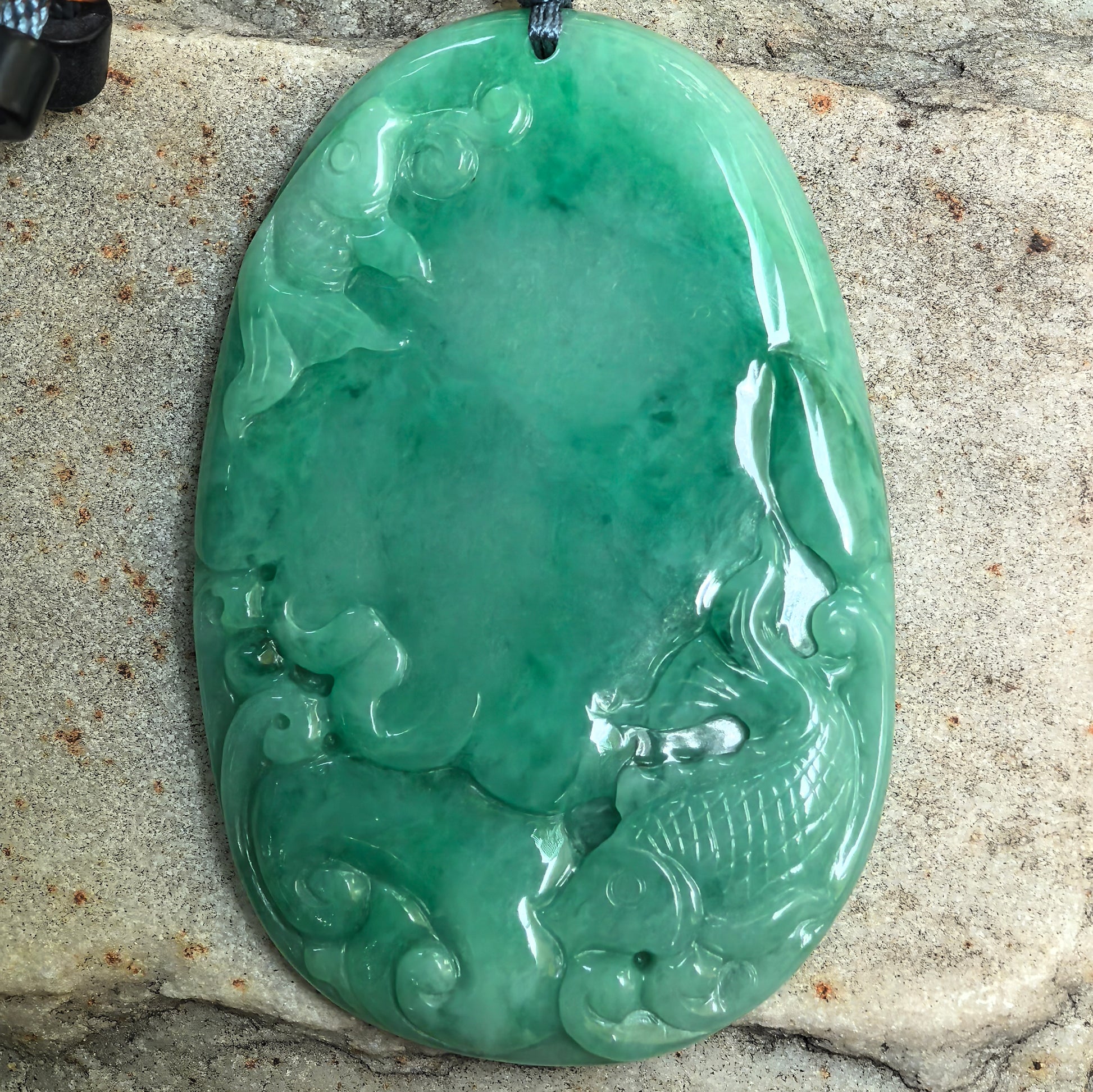 Close-up of natural green jadeite fish plaque pendant showing glossy glutinous texture and carved details.