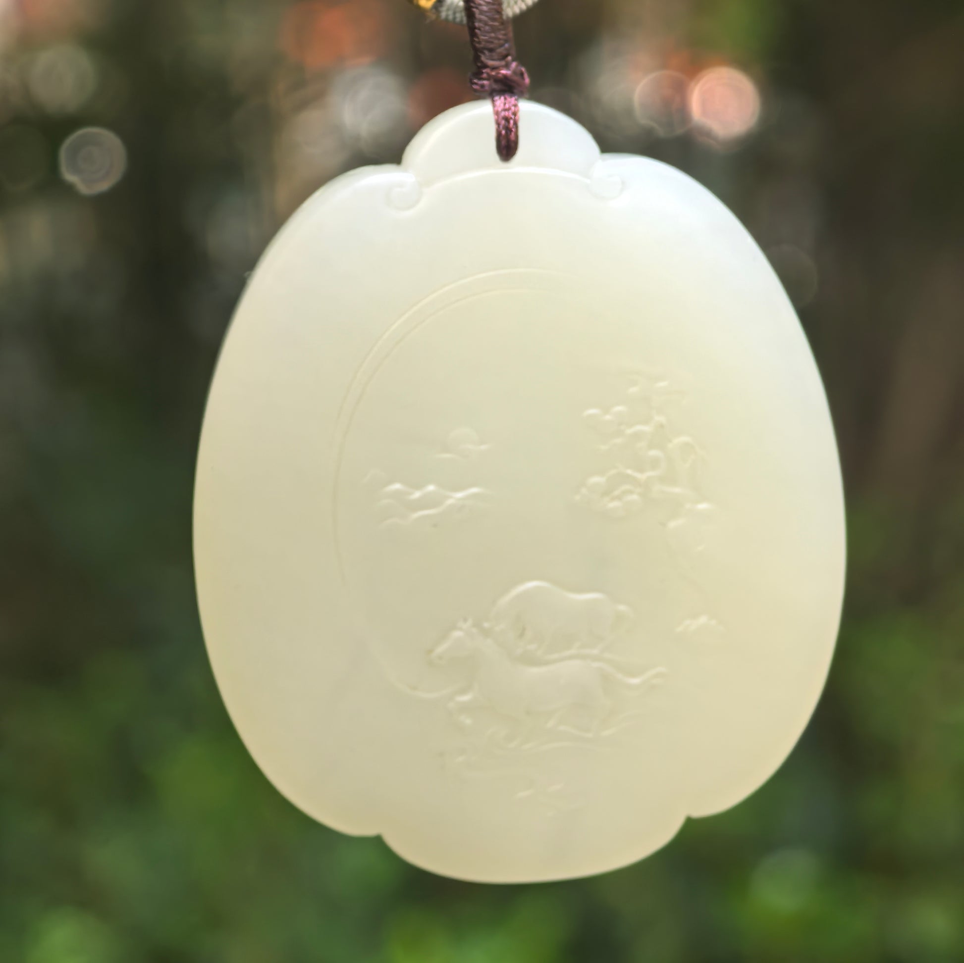 Natural Hetian jade greenish-white horse plaque pendant hanging against a soft green background.