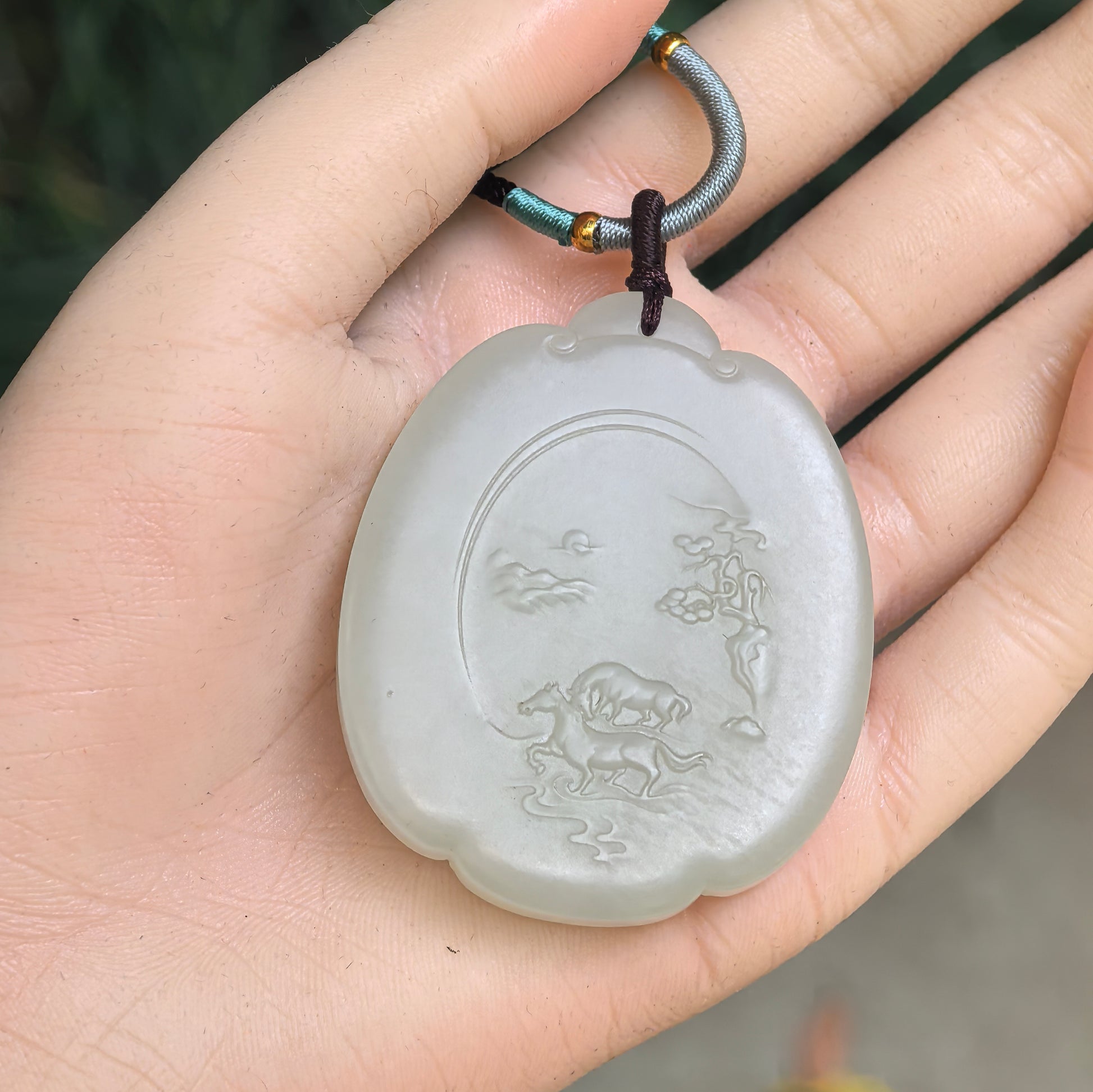 Large Hetian jade horse plaque pendant shown in hand with carved landscape motif.