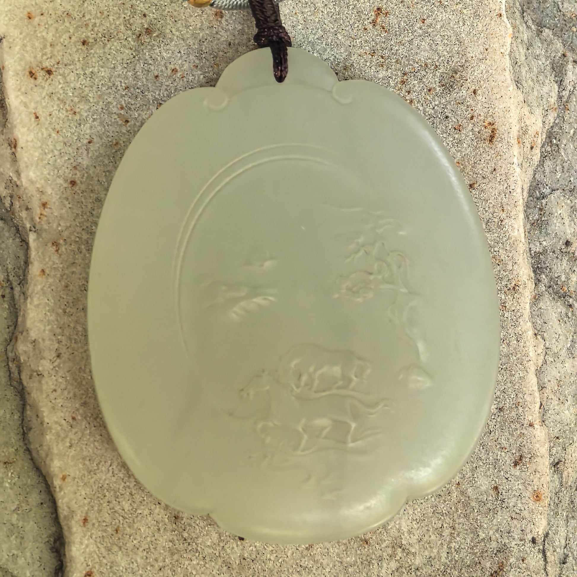 Close-up of greenish-white Hetian jade pendant with horses, mountains, clouds, and tree carving.