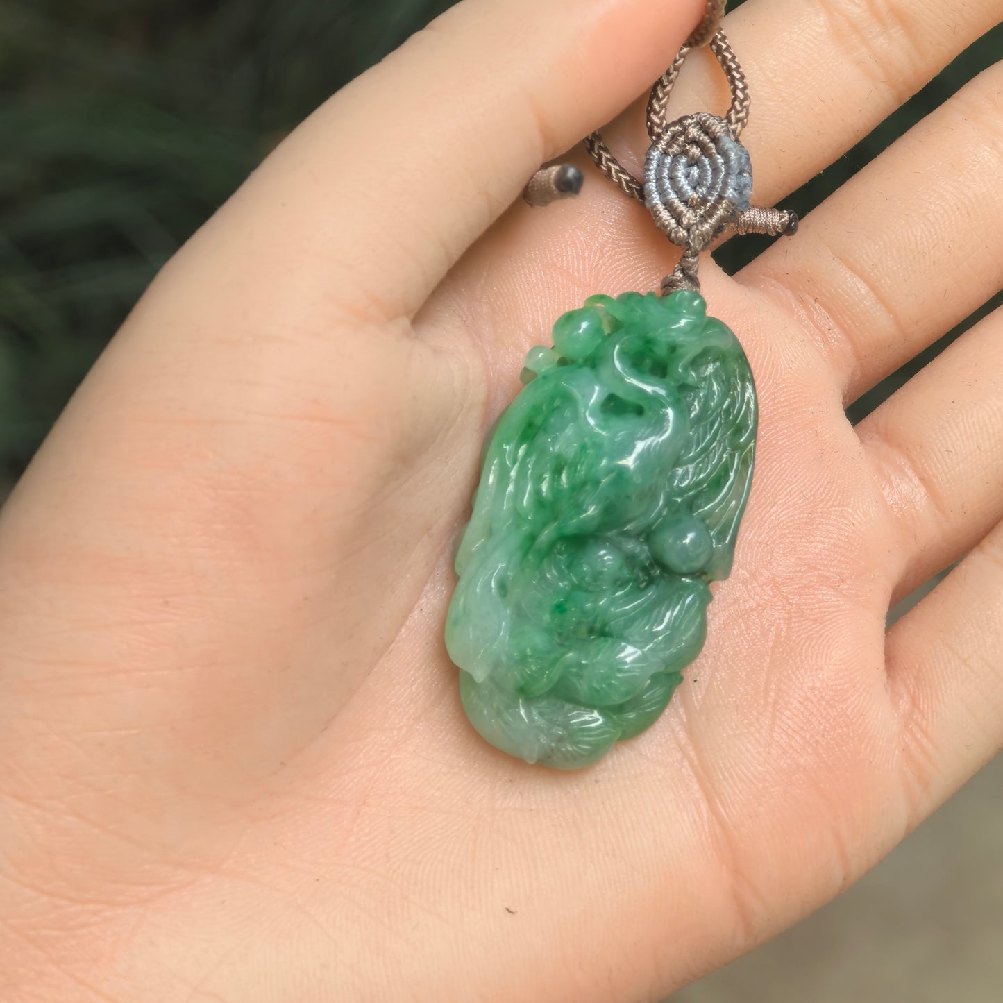 Green jadeite phoenix pendant displayed in hand, showing detailed carving and smooth polished luster.