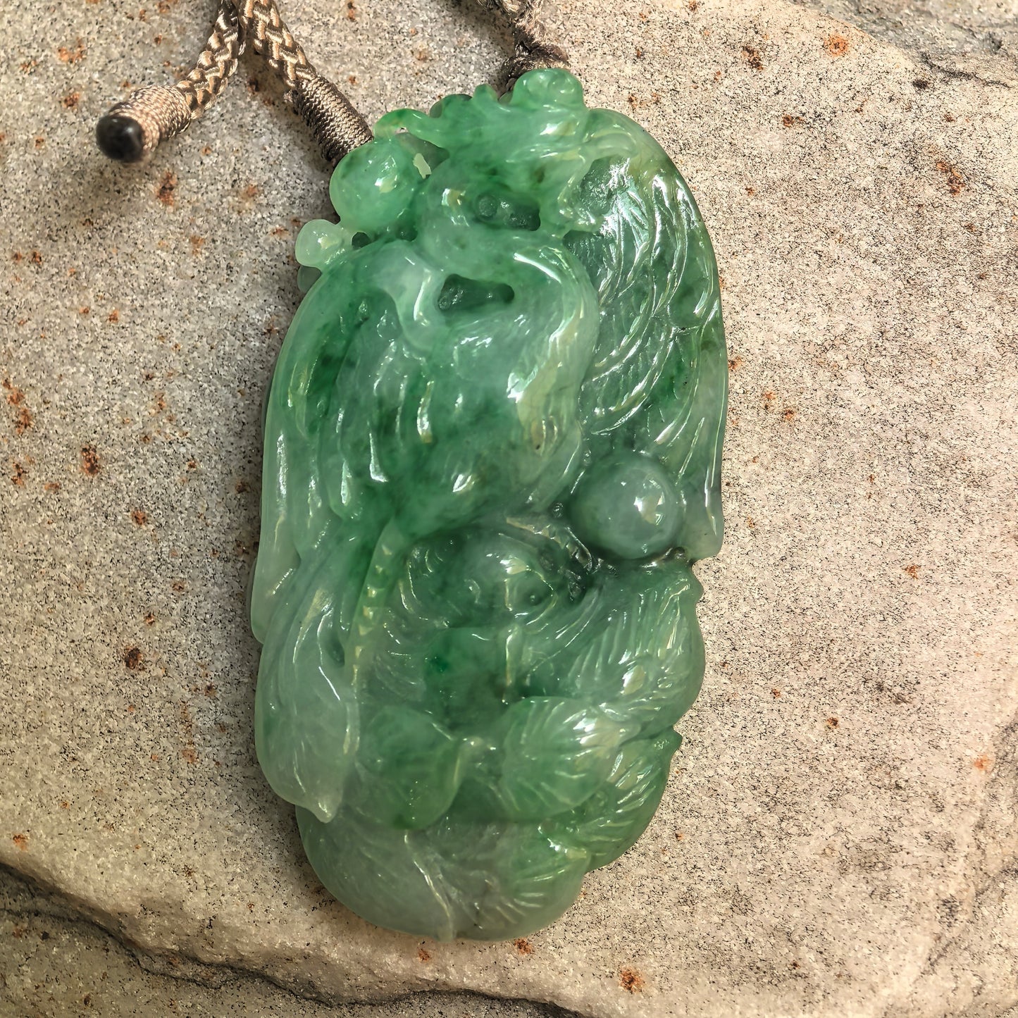 Close-up of carved jadeite phoenix pendant showing raised feather details and natural green color variation.