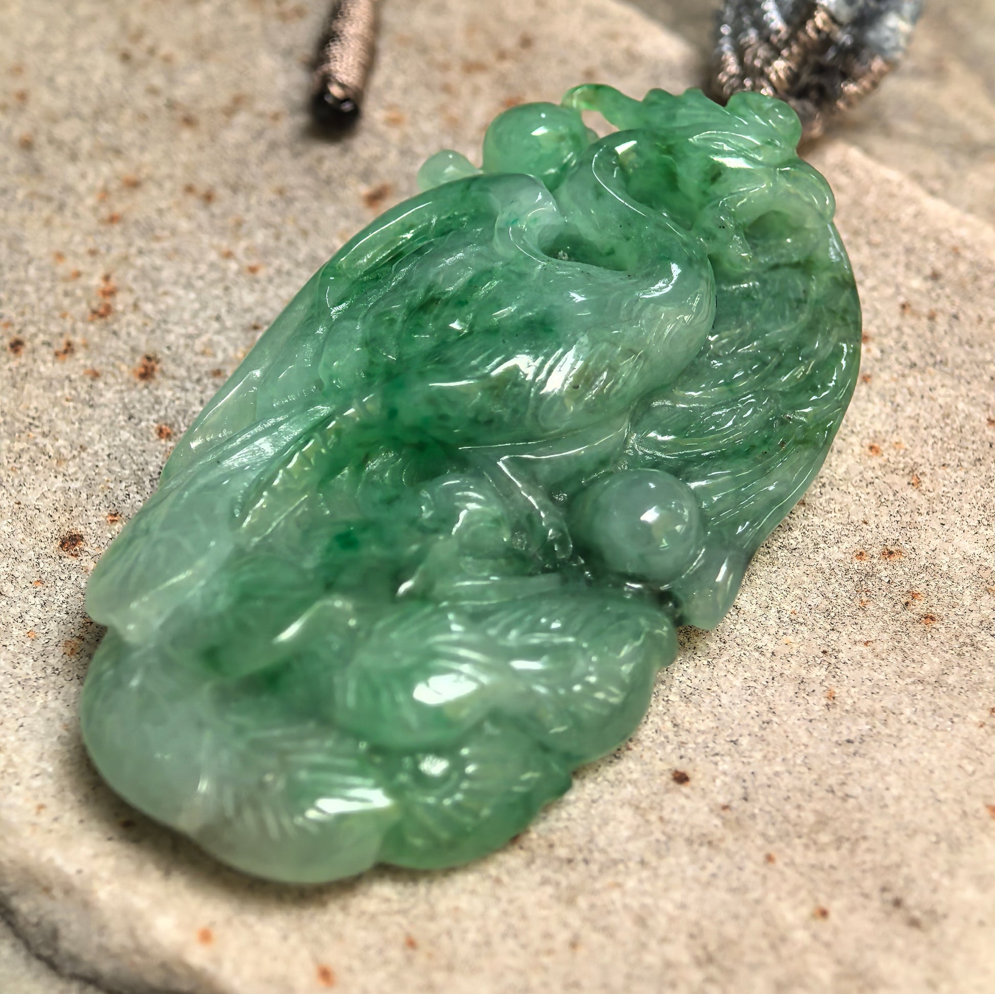 Side view of green jadeite phoenix pendant showing thickness, rounded carving, and three-dimensional structure.