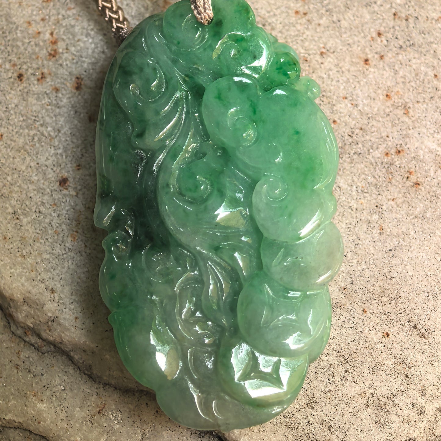 Double-sided carved Natural Grade-A green jadeite phoenix pendant displayed on stone surface.