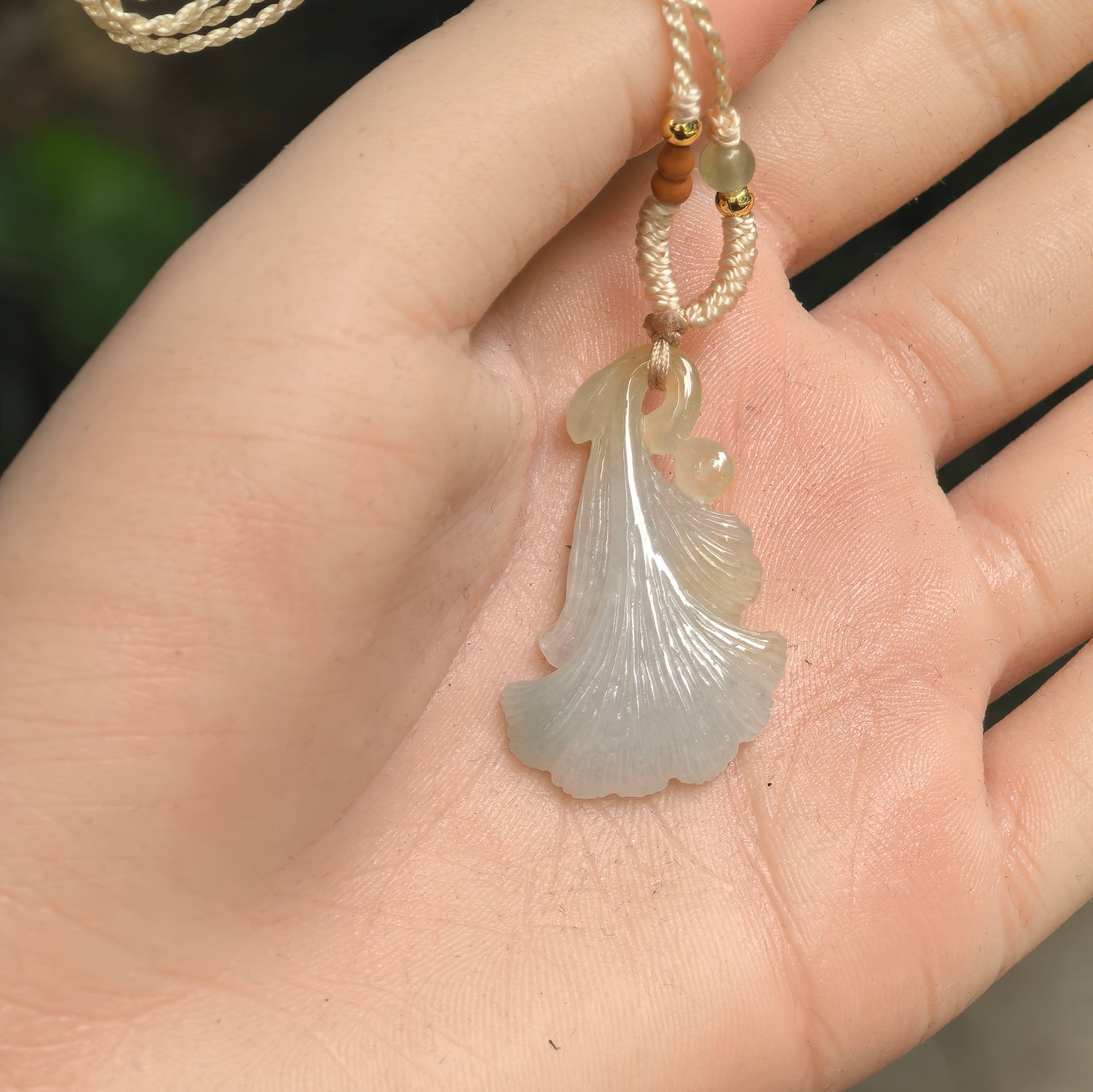 Light green ginkgo leaf jadeite pendant shown in hand with fine fan-like leaf carving and polished luster.