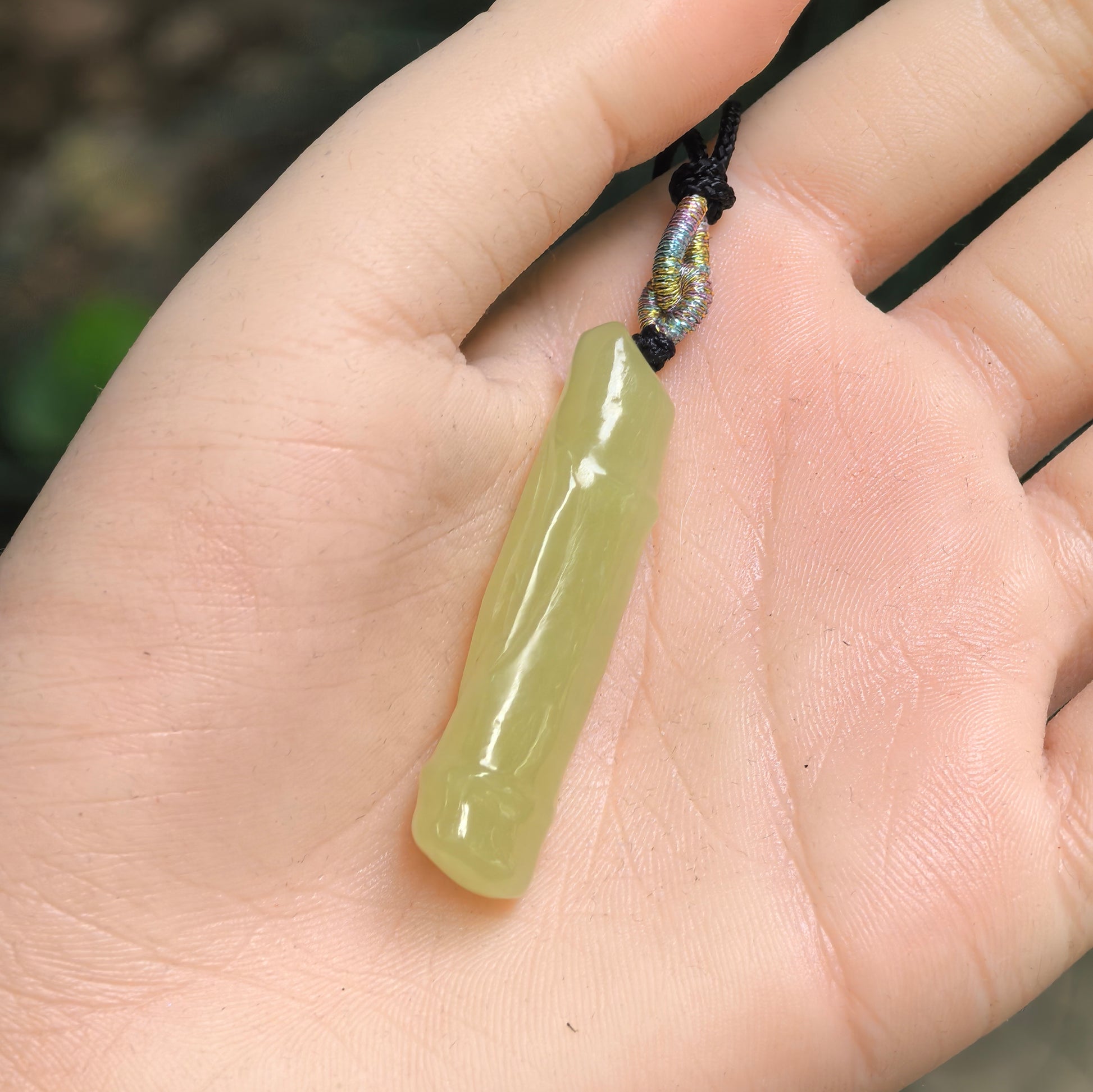 Yellow-green Hetian jade bamboo pendant shown in hand with slim elongated shape.