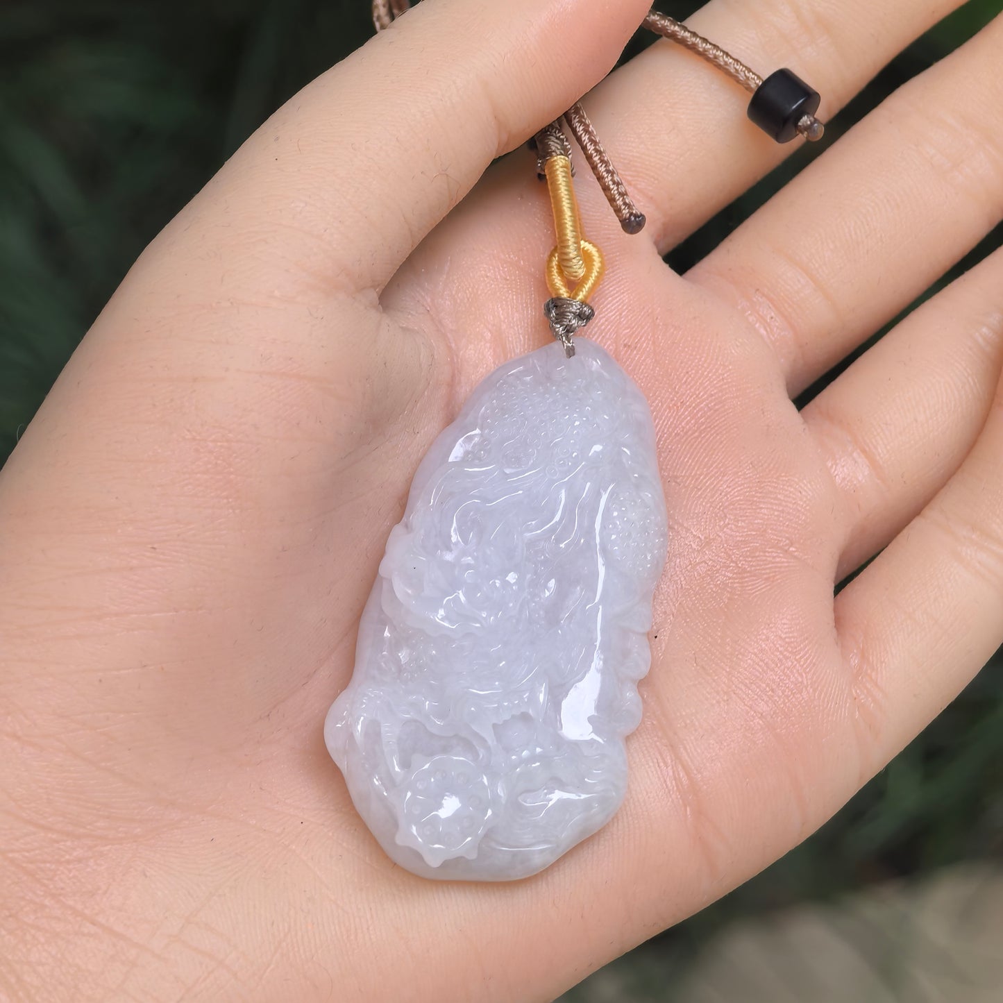 White jadeite dragon pendant shown in hand with raised carved details.