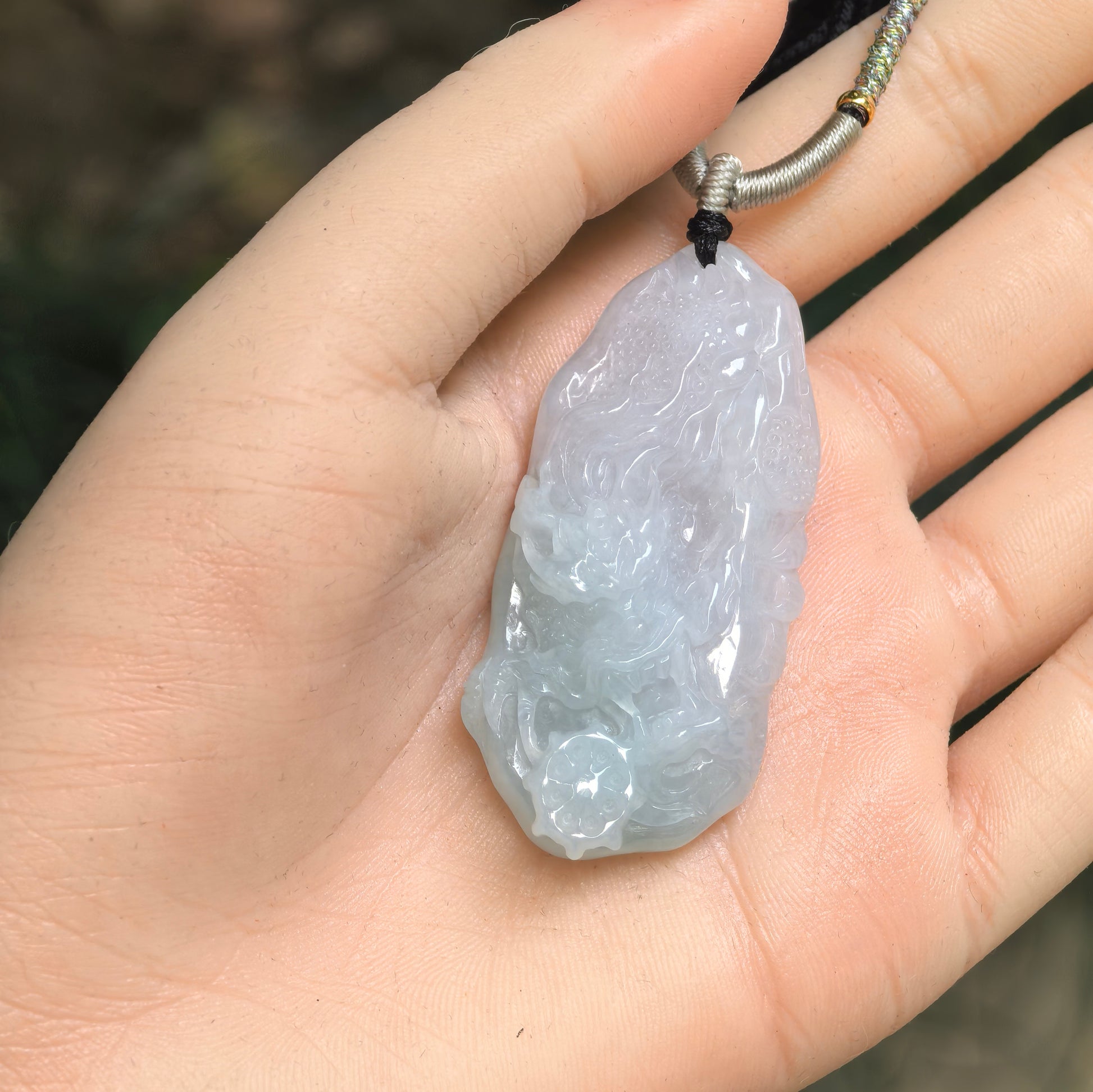Pale green jadeite dragon pendant shown in hand with raised carved details.