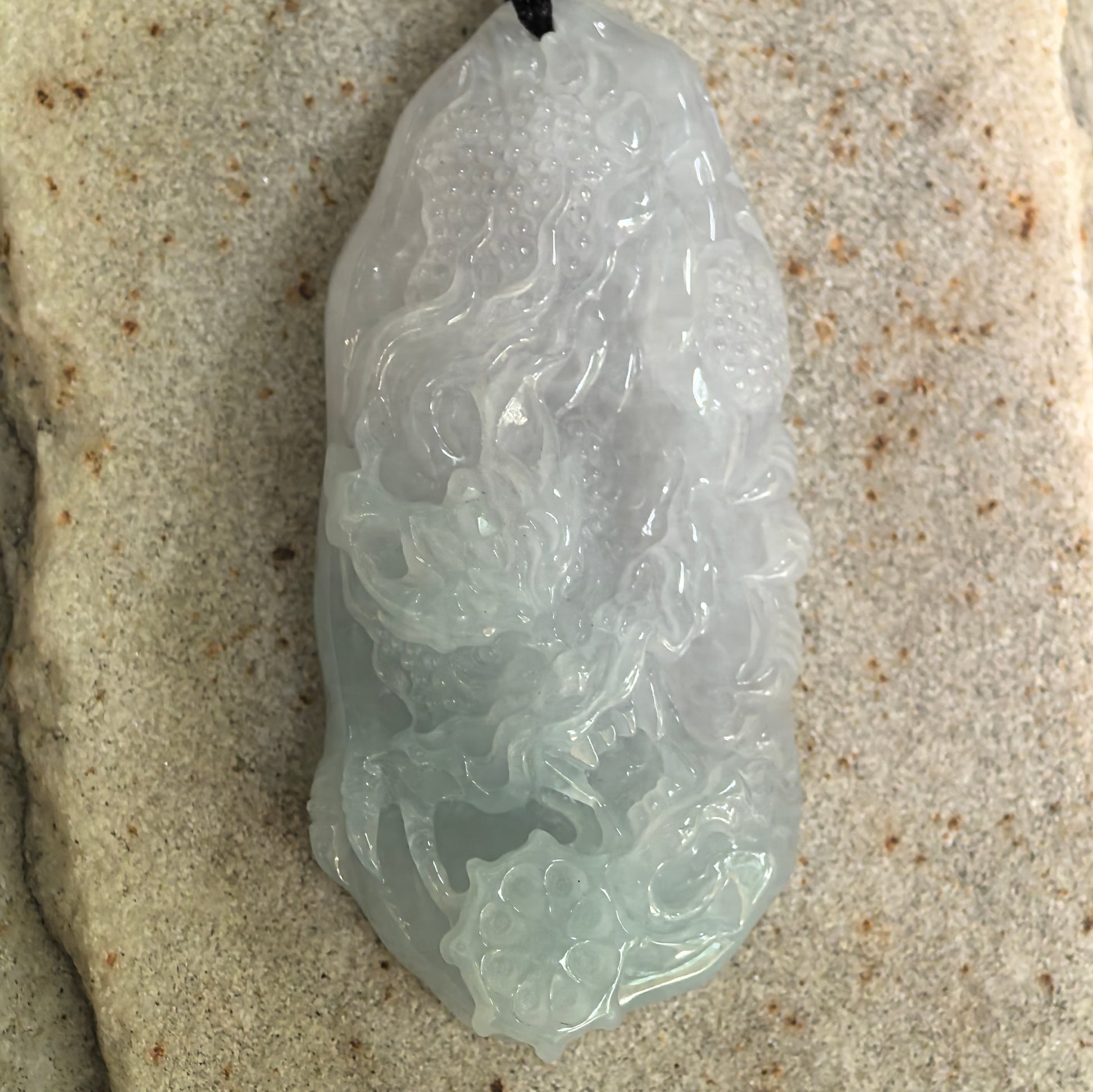 Close-up of carved jadeite dragon pendant showing smooth polish and soft translucency.