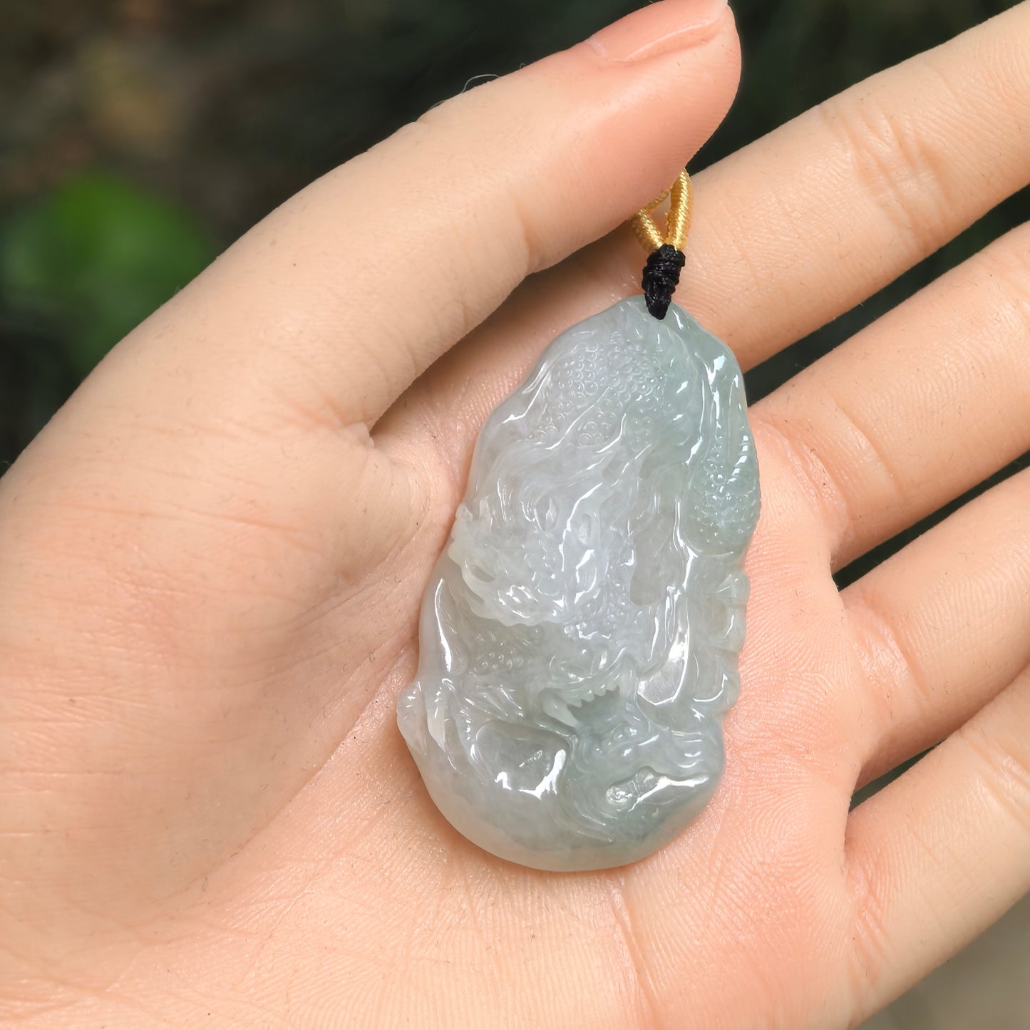 Pale green jadeite dragon pendant shown in hand with raised carved details.