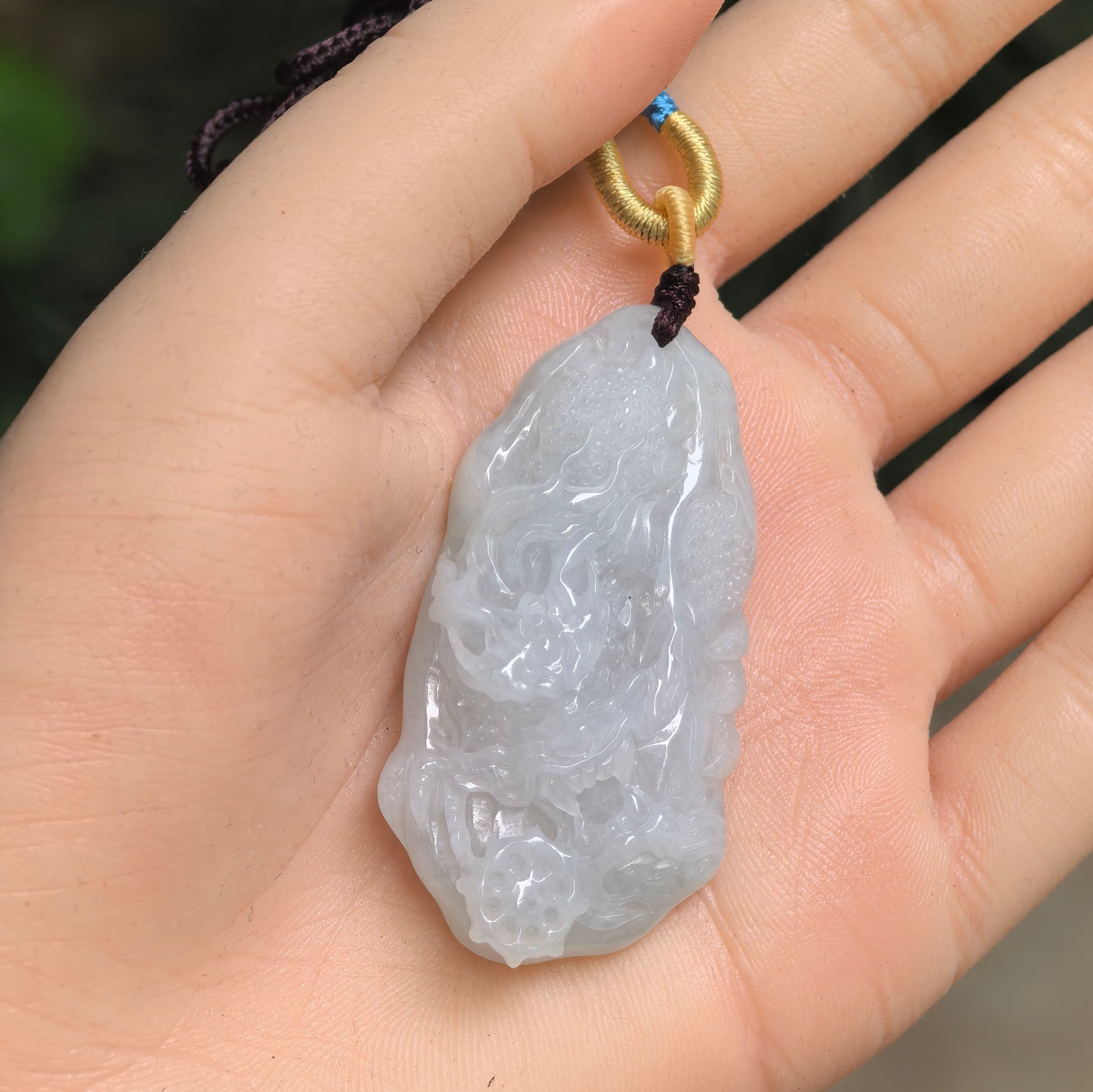 Pale green jadeite dragon pendant shown in hand with raised carved details.
