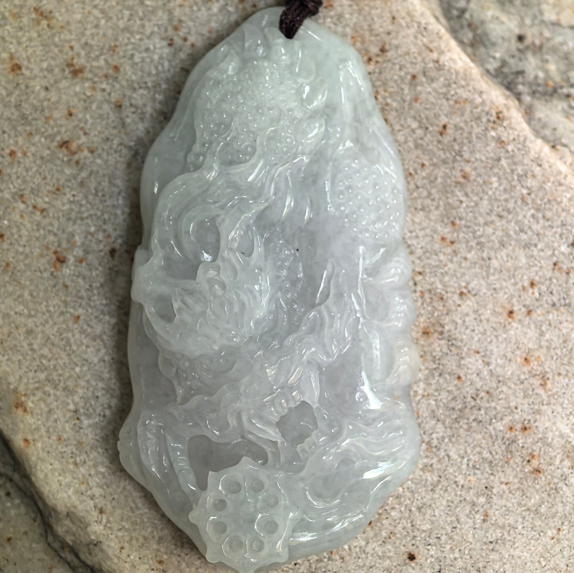 Close-up of carved jadeite dragon pendant showing smooth polish and soft translucency.
