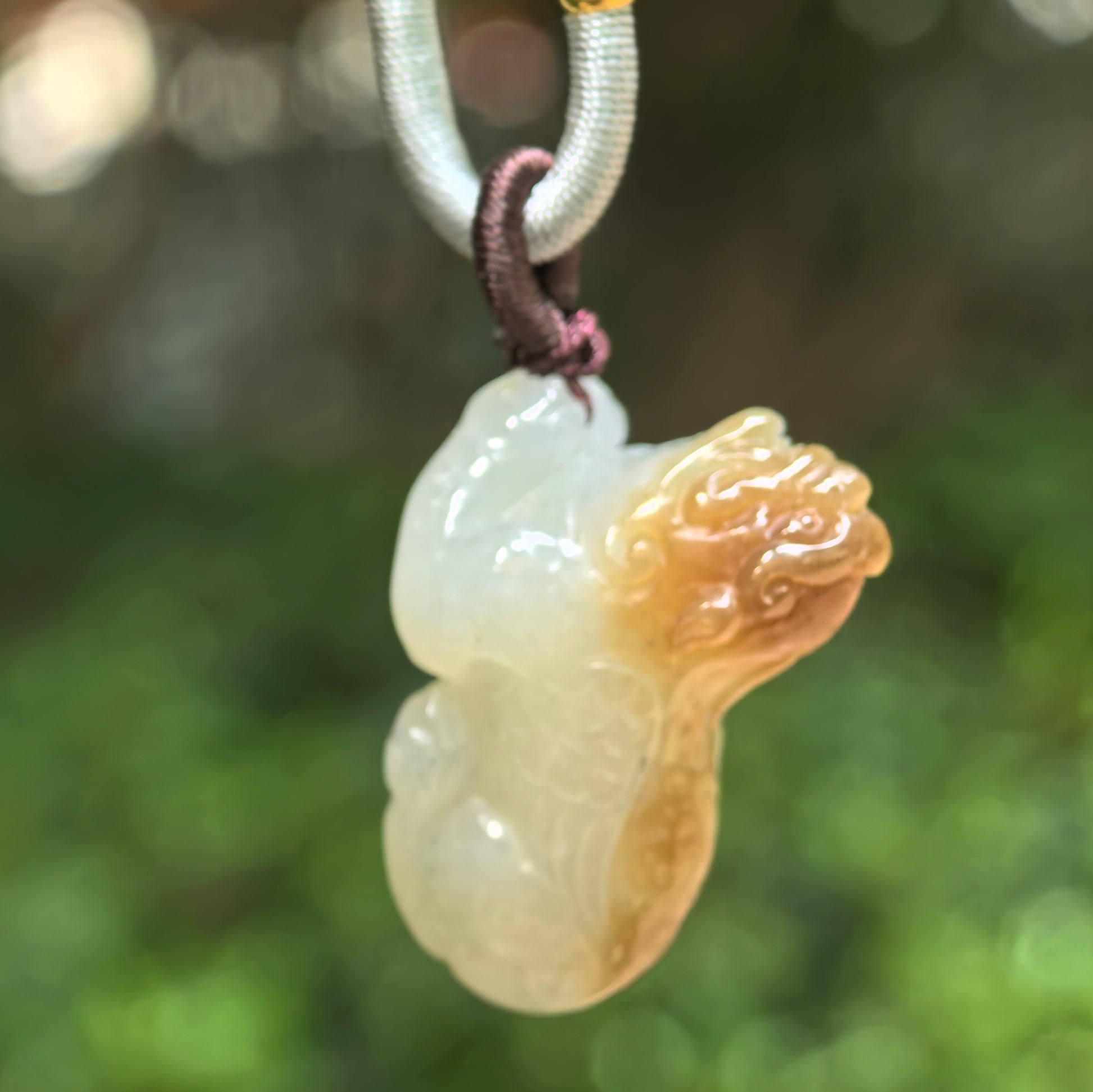 Natural Hetian jade sugar-brown Pixiu pendant hanging against a green background.