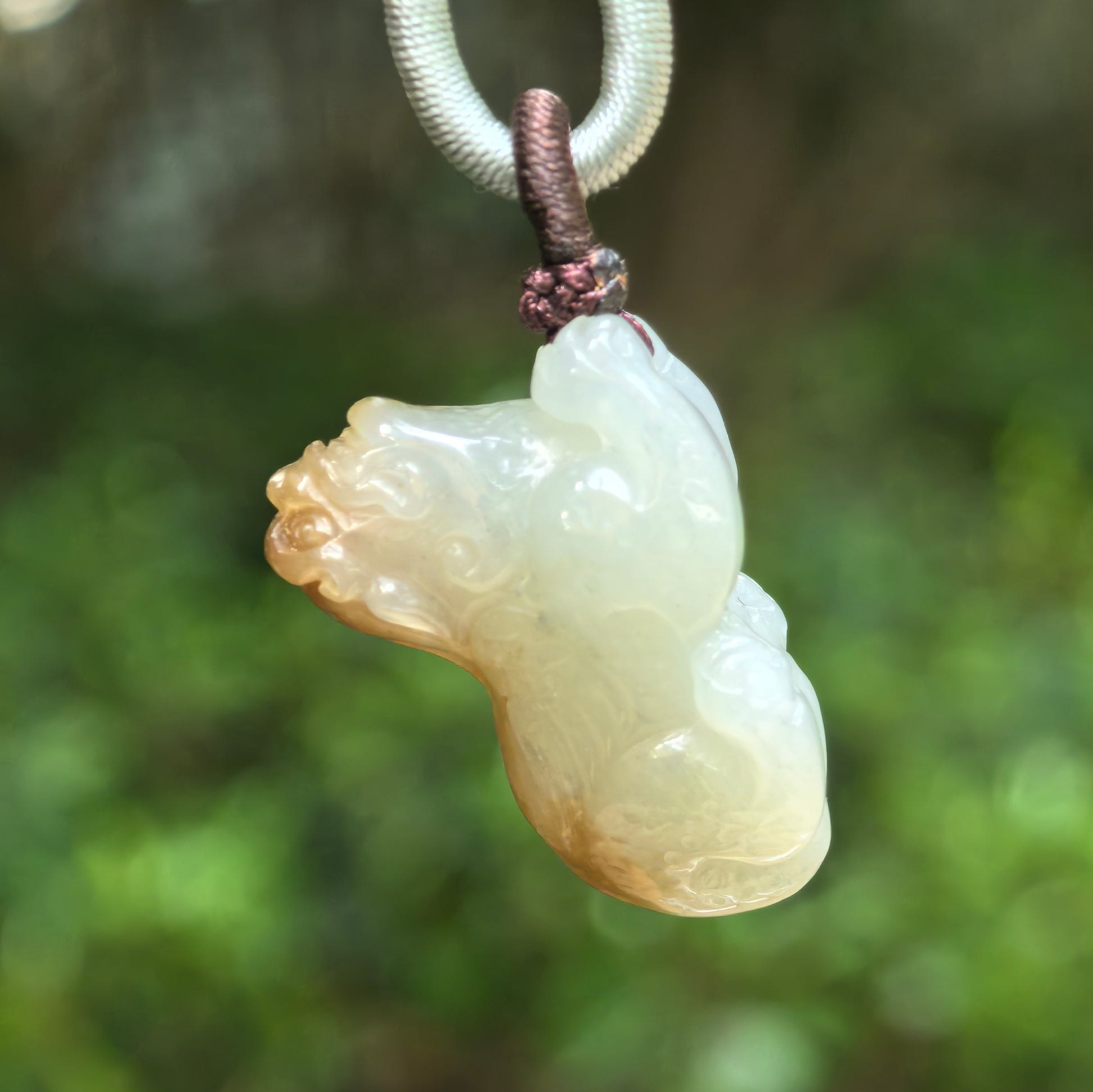 Side view of greenish-white Hetian jade Pixiu pendant with natural sugar-brown head.
