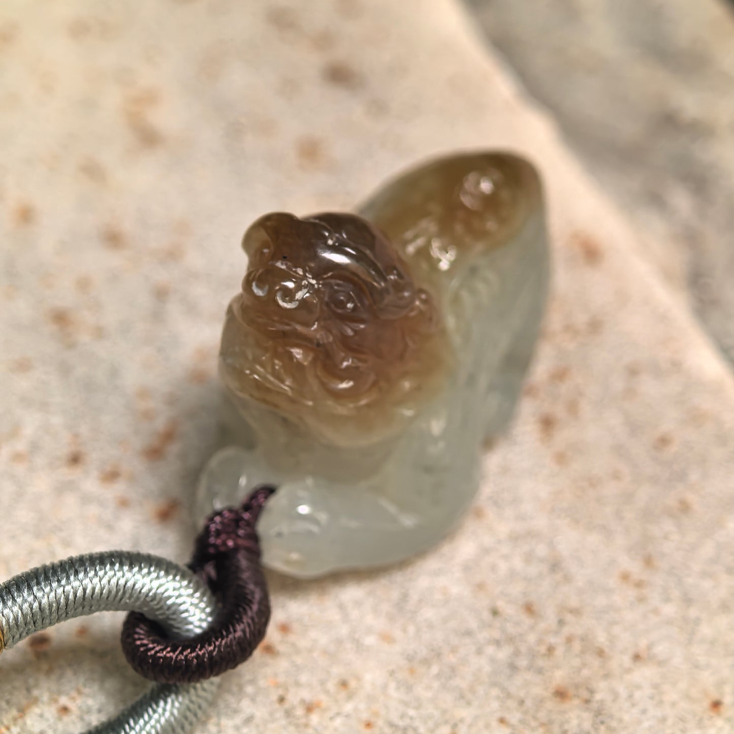 Natural Hetian jade Pixiu pendant displayed on stone surface with compact three-dimensional carving.
