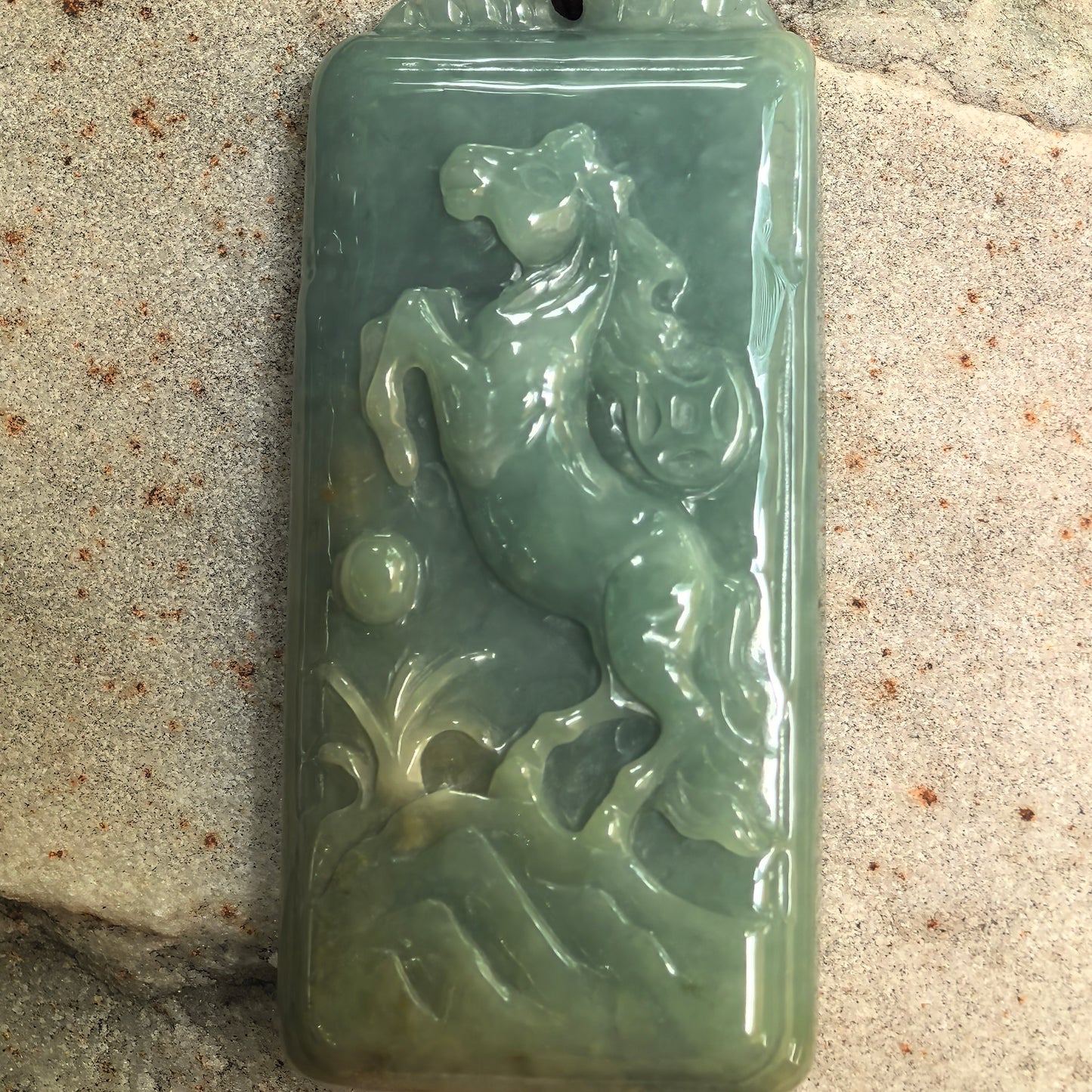 Close-up of carved jadeite horse pendant showing flowing mane, lifted front leg, and rounded decorative details.