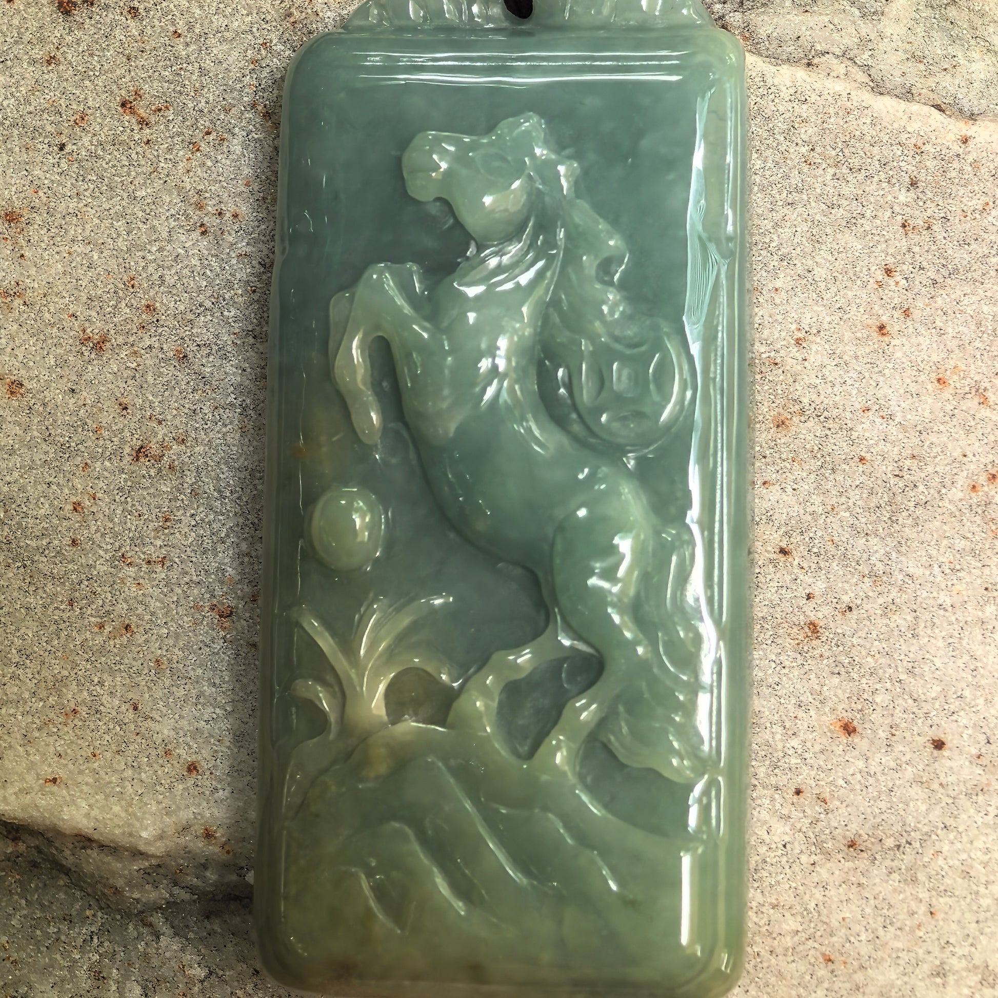 Close-up of carved jadeite horse pendant showing flowing mane, lifted front leg, and rounded decorative details.