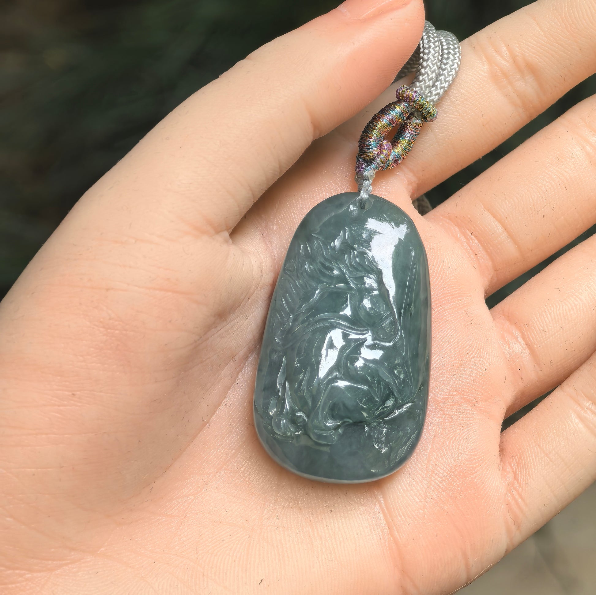 Deep green jadeite horse pendant shown in hand with bold carved details.