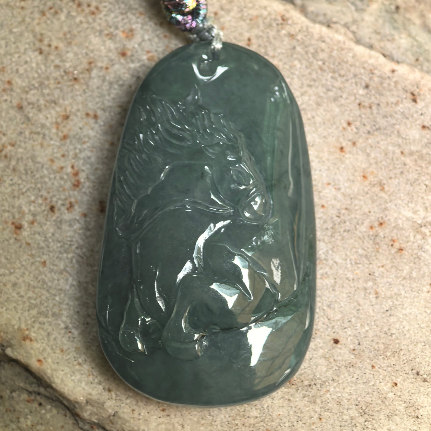 Close-up of carved horse jadeite pendant showing smooth polish and deep green tone.
