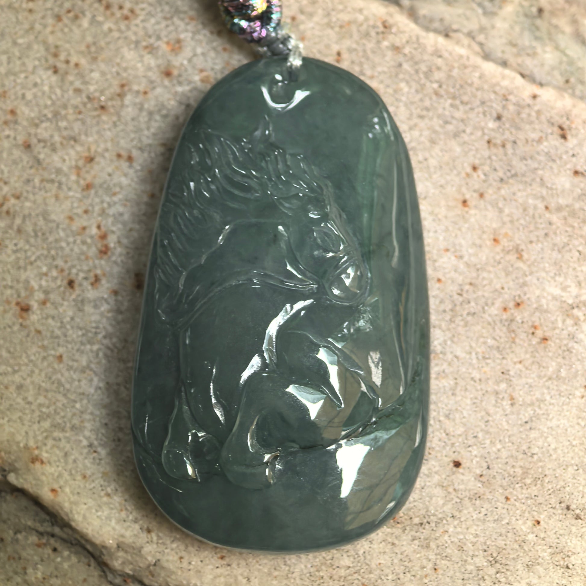 Close-up of carved horse jadeite pendant showing smooth polish and deep green tone.