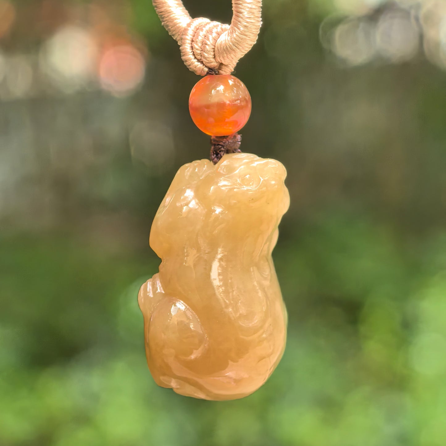 Natural Hetian jade sugar brown Pixiu pendant hanging against a soft green background.
