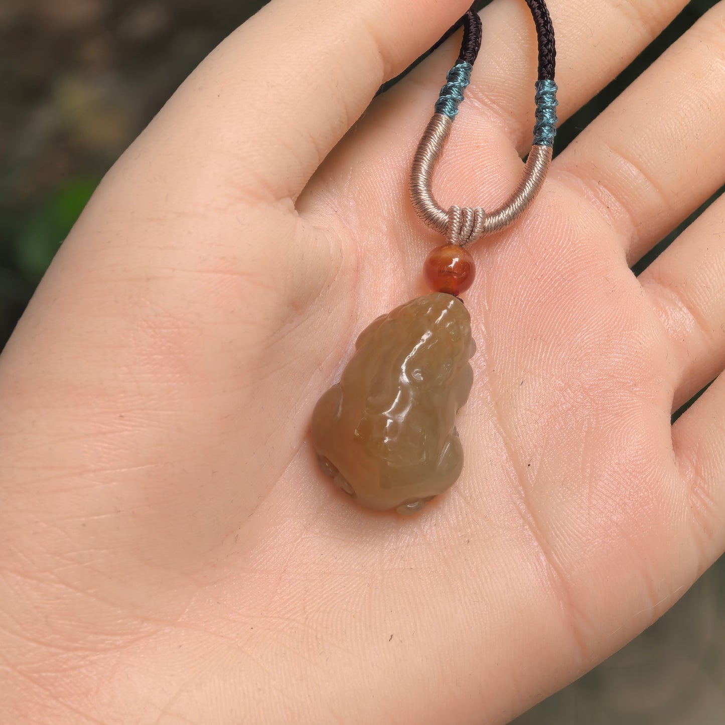 Three-dimensional sugar-brown Hetian jade Pixiu pendant shown in hand with compact rounded form.