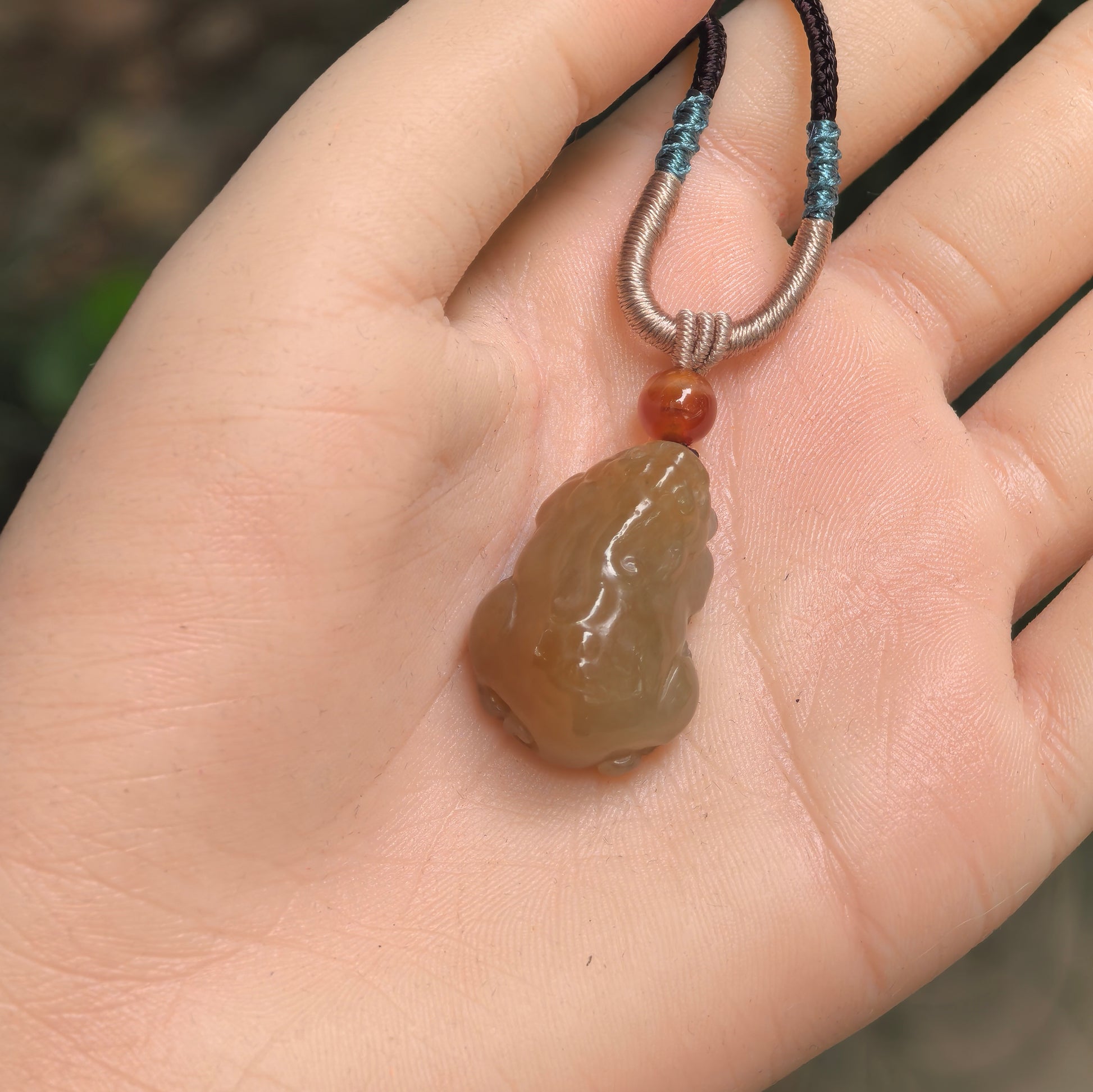 Three-dimensional sugar-brown Hetian jade Pixiu pendant shown in hand with compact rounded form.