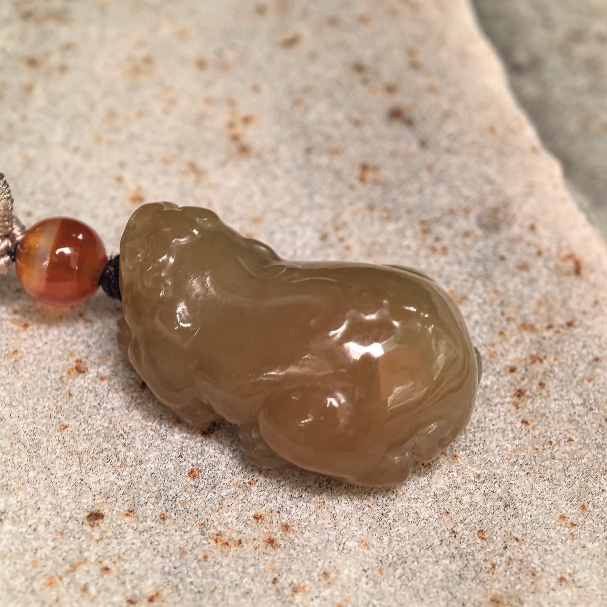 Side view of 3D carved Hetian jade Pixiu pendant showing thick sculptural shape.