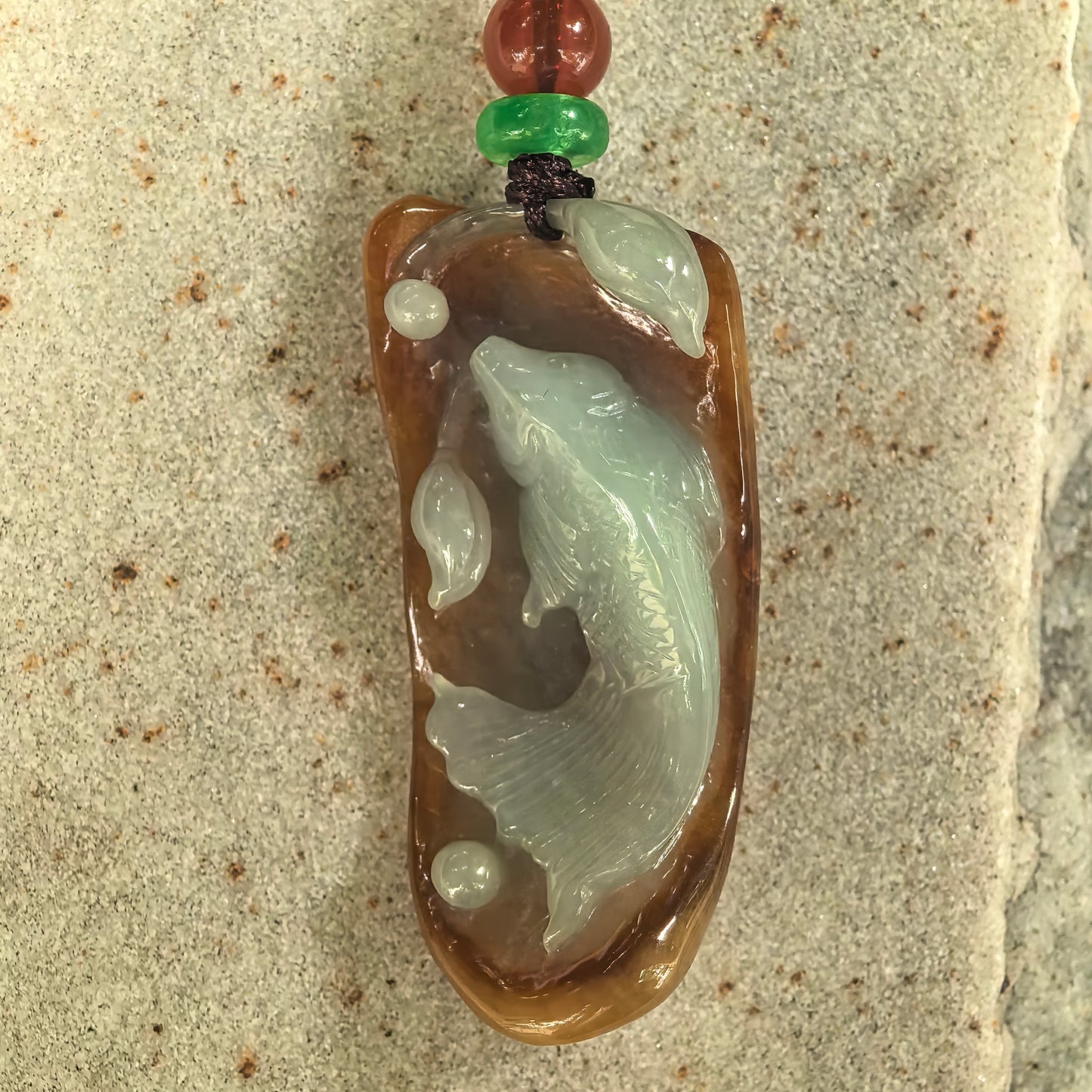 Close-up of jadeite fish pendant showing raised fish carving, leaf details, and glossy polish.
