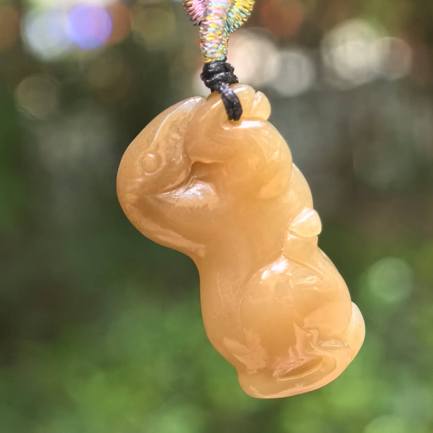 Natural Hetian jade sugar brown horse pendant hanging against a soft green background.