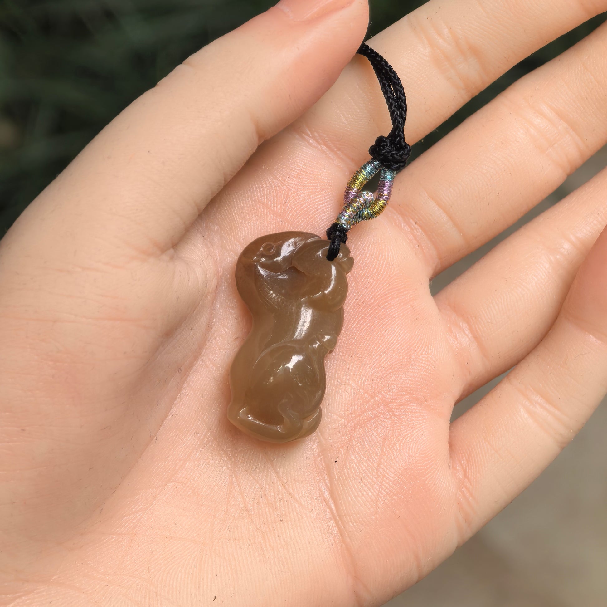 Three-dimensional sugar-brown Hetian jade horse pendant shown in hand with compact rounded form.