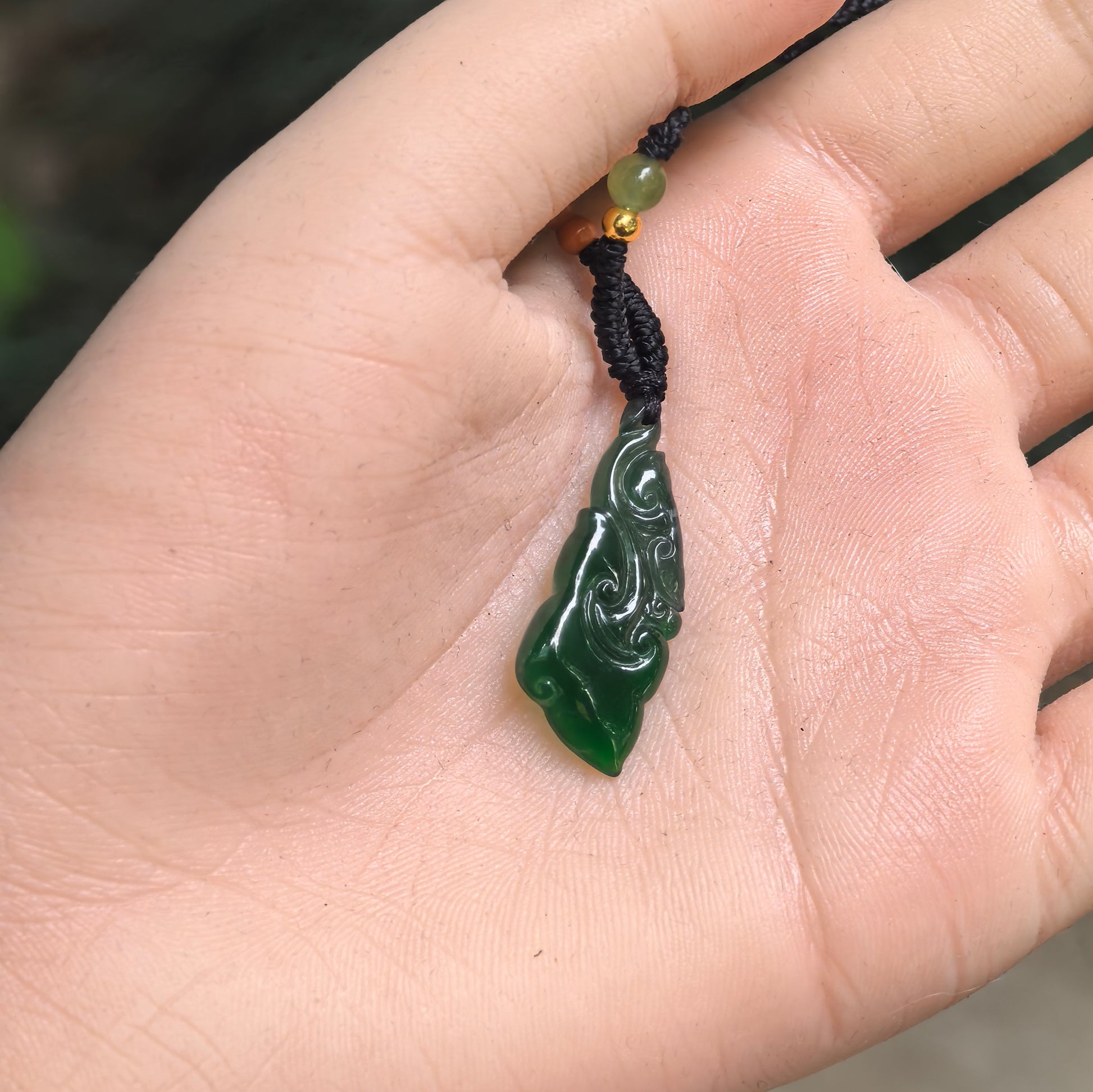Small dark green jadeite Ruyi pendant shown in hand with glossy polished surface and curved carving.