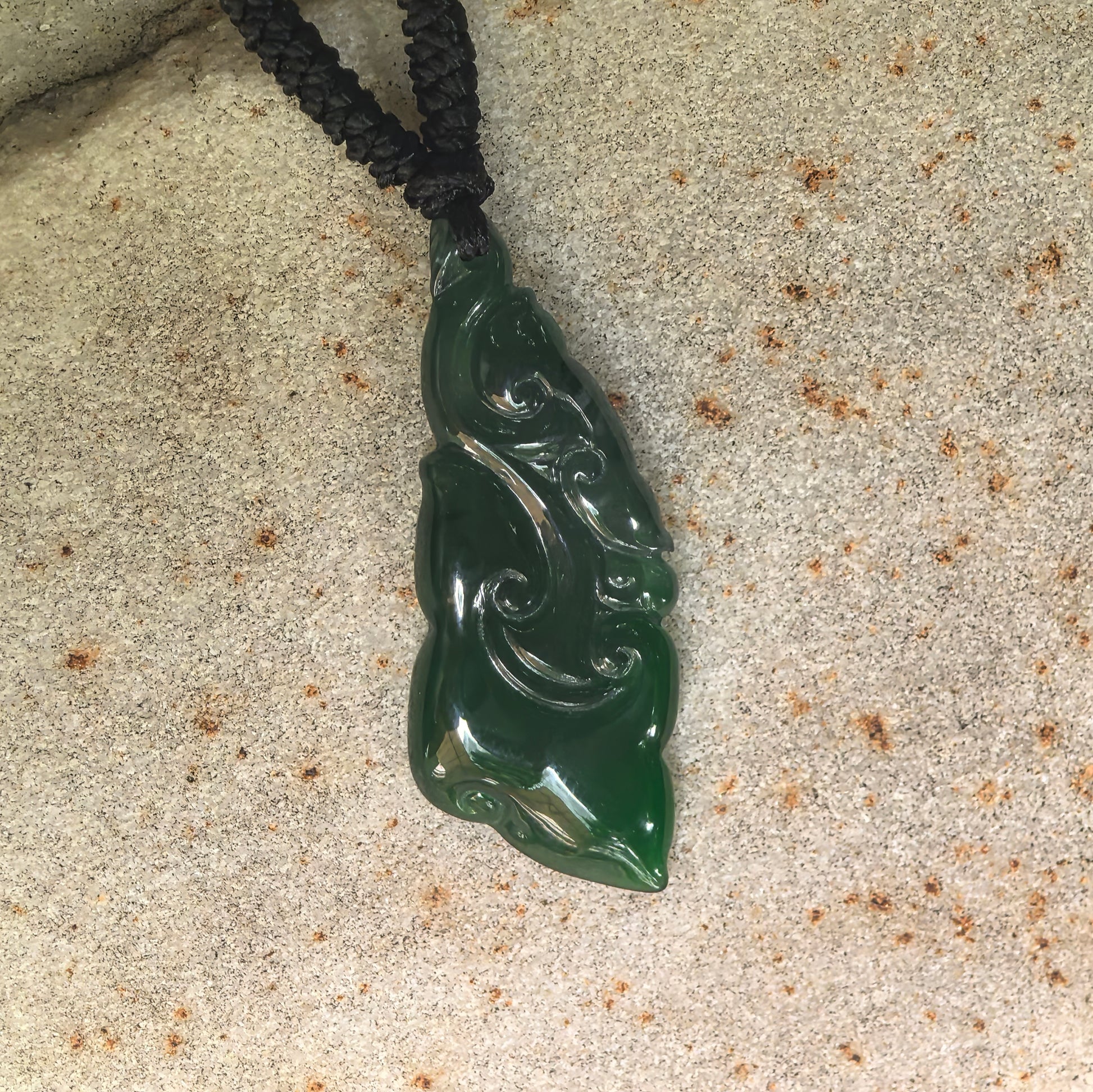 Close-up of vivid green Guatemalan jadeite Ruyi pendant showing raised cloud-like carved lines.