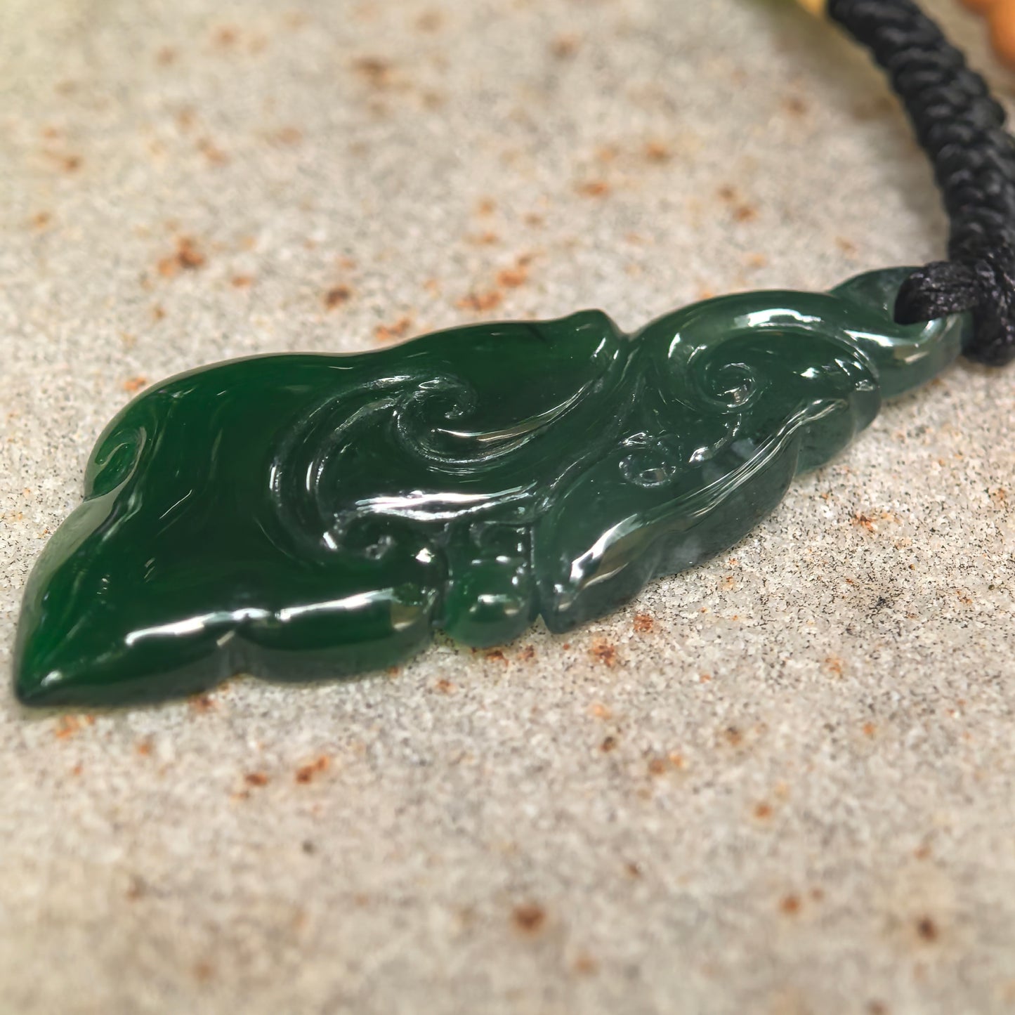 Side view of slender jadeite Ruyi pendant showing slim 3 mm thickness and translucent dark green body.