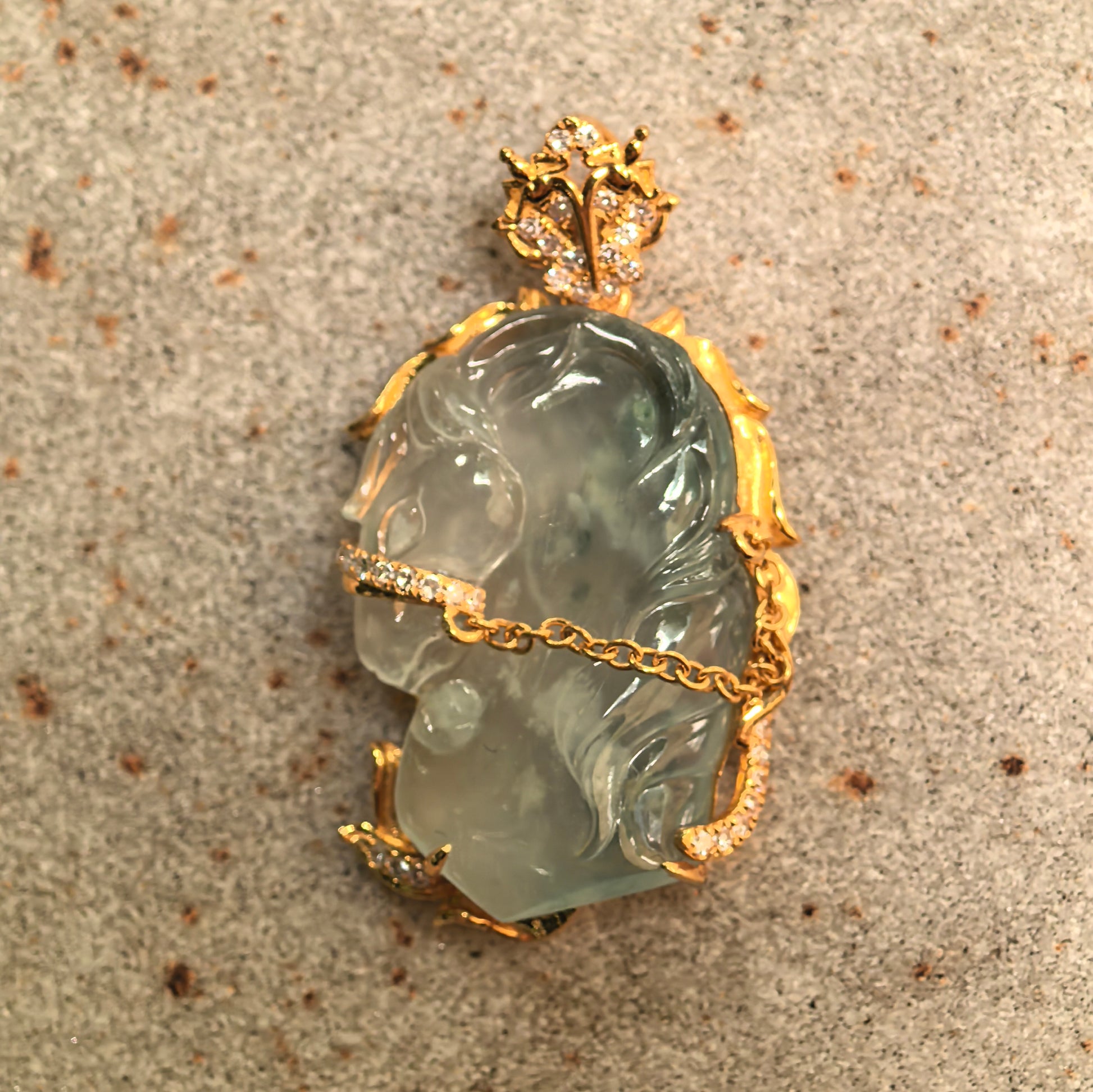 Natural Grade-A icy light green horse head jadeite pendant with 18K gold setting shown on display surface.