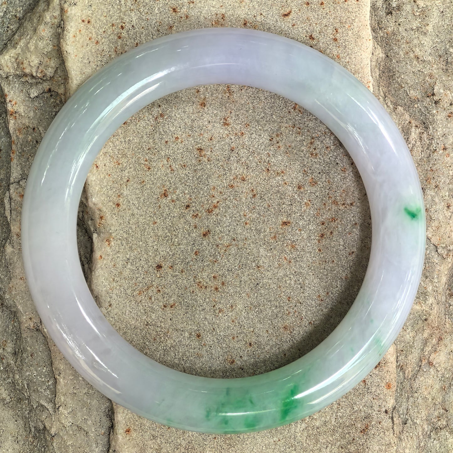 Round jadeite bangle displayed on stone surface highlighting circular shape and polished finish.
