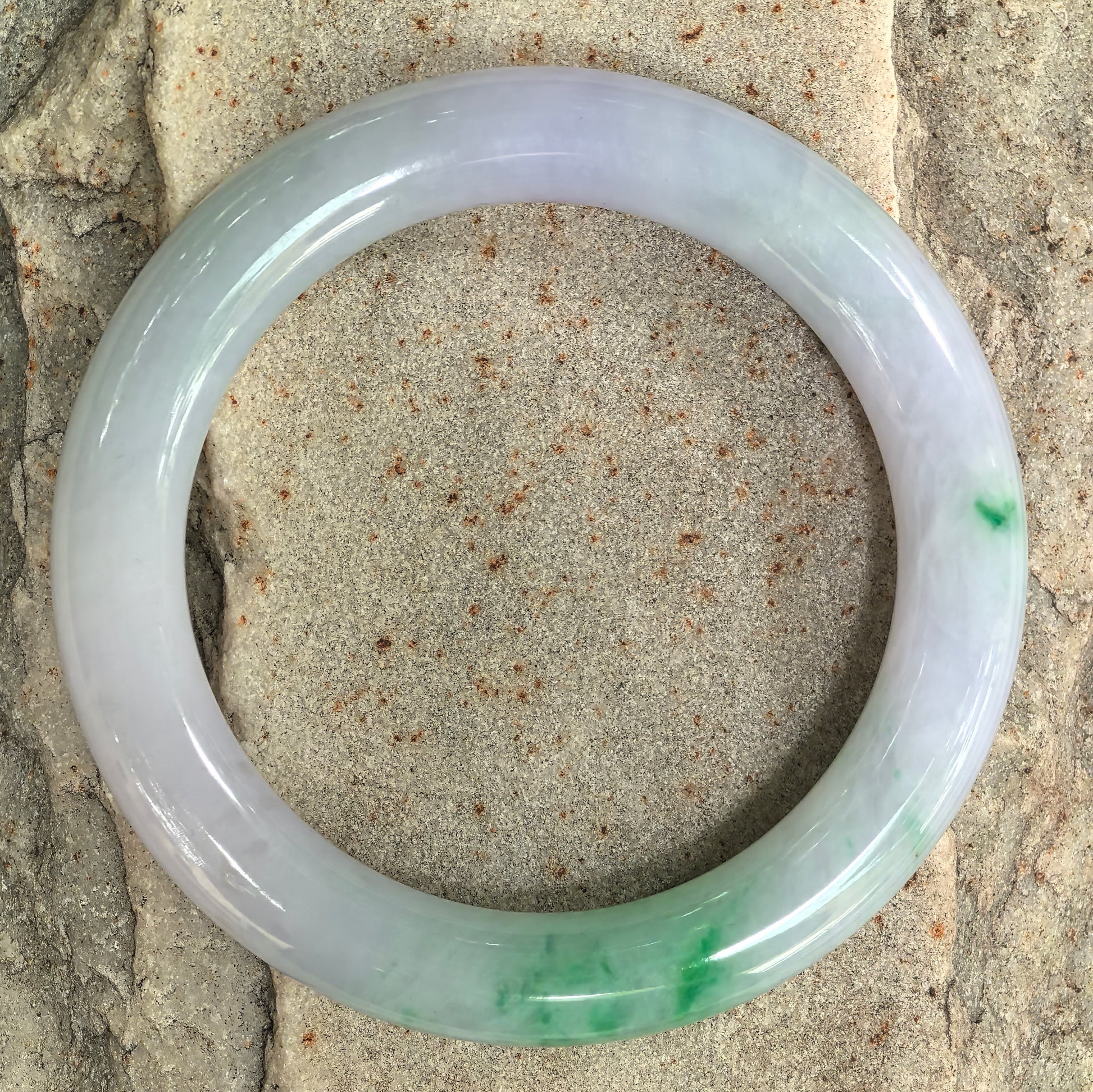 Round jadeite bangle displayed on stone surface highlighting circular shape and polished finish.
