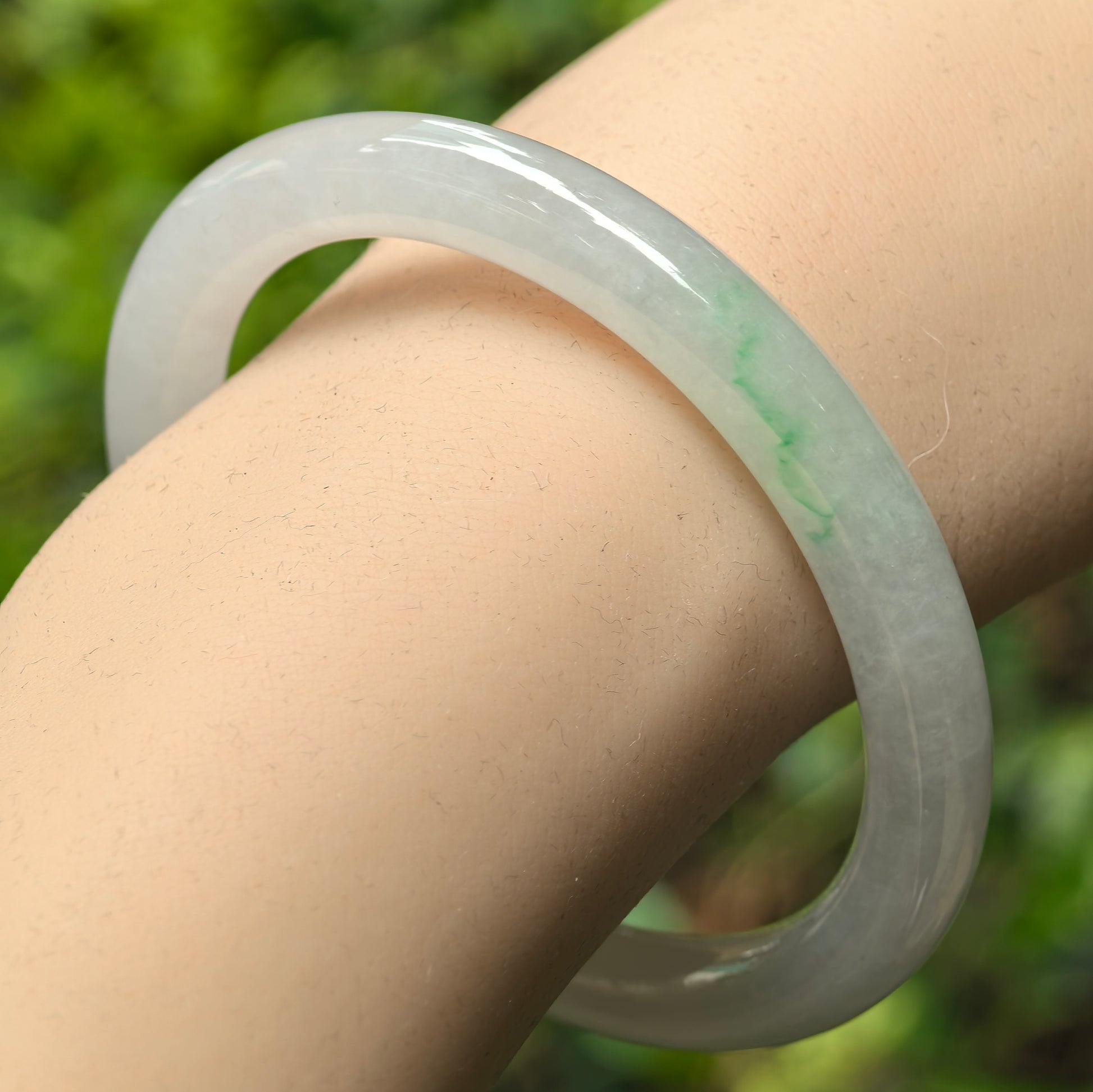 Natural Grade-A icy glutinous light white jadeite round-bar bangle with faint green accent shown on wrist, highlighting smooth translucent surface.

